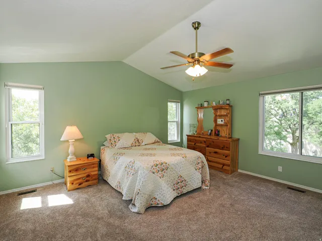 Vaulted ceiling, ceiling fan with integrated lighting, multiple windows, and carpeted flooring