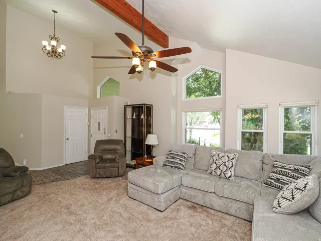 Spacious great room showcasing vaulted ceilings with exposed wood beams, a ceiling fan with integrated lighting, and abundant natural light from multiple large windows