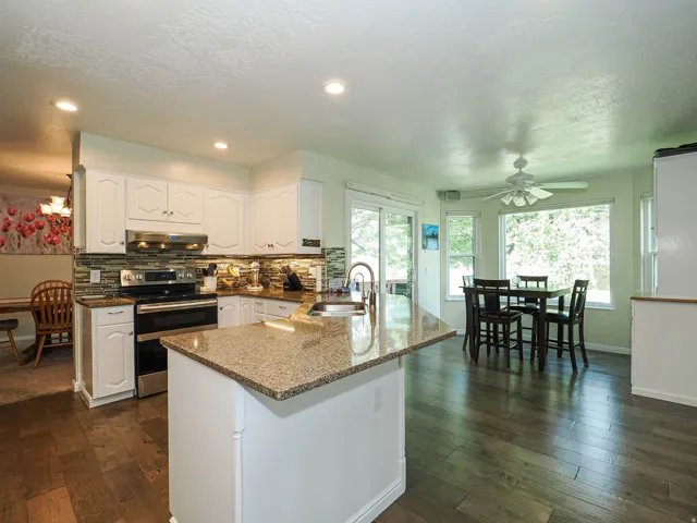 Kitchen featuring white cabinetry, stone countertops, a tile backsplash, stainless steel appliances, and wood-finish flooring