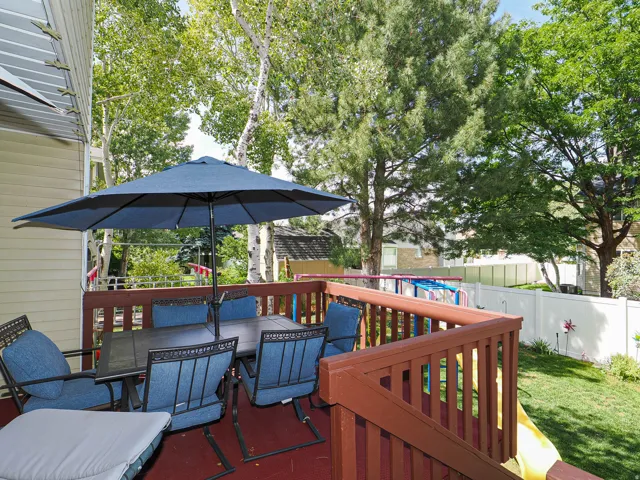 Spacious outdoor deck with wood railing, leading to a manicured lawn and mature trees