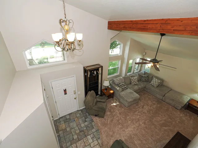 Vaulted ceiling with an exposed wood beam, decorative chandelier, and multiple windows