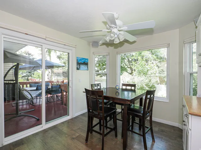Wood-finish flooring, sliding glass patio door, bay window, ceiling fan with light fixture, and white cabinetry with wood countertop