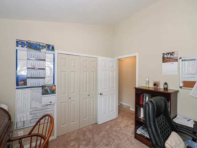Neutral-toned carpeting, vaulted ceiling, and interior door with white trim