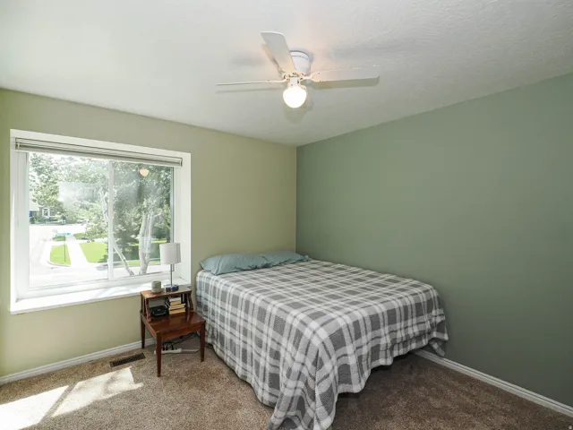 Carpeted room with a large window, a ceiling fan with integrated lighting, and painted walls