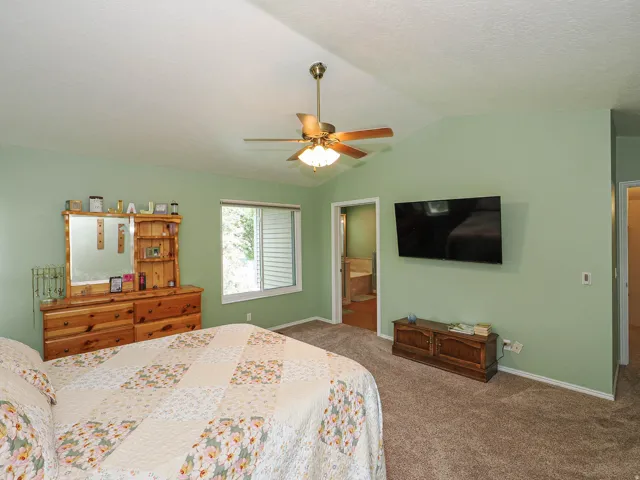 Vaulted ceiling with a ceiling fan, plush carpet flooring, a window with horizontal blinds, and a wall-mounted television