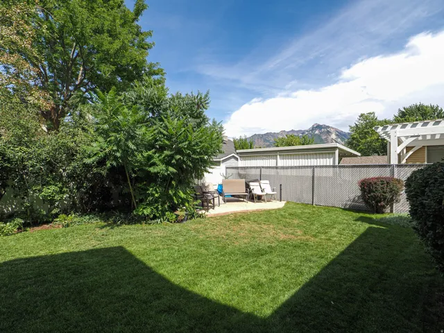 Expansive backyard featuring a manicured lawn, mature shade trees, and metal storage shed with covered patio area