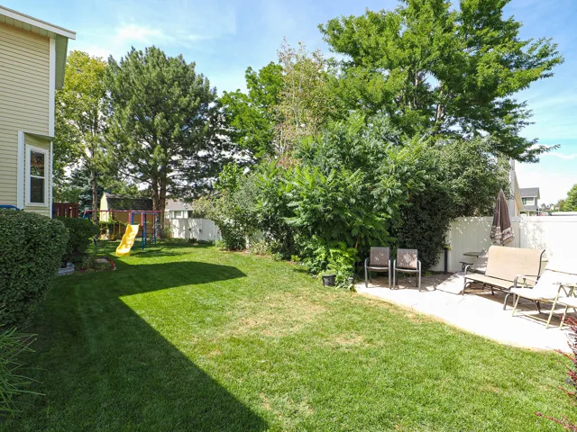 Expansive backyard featuring a lush lawn, mature trees, a concrete patio, and a privacy fence