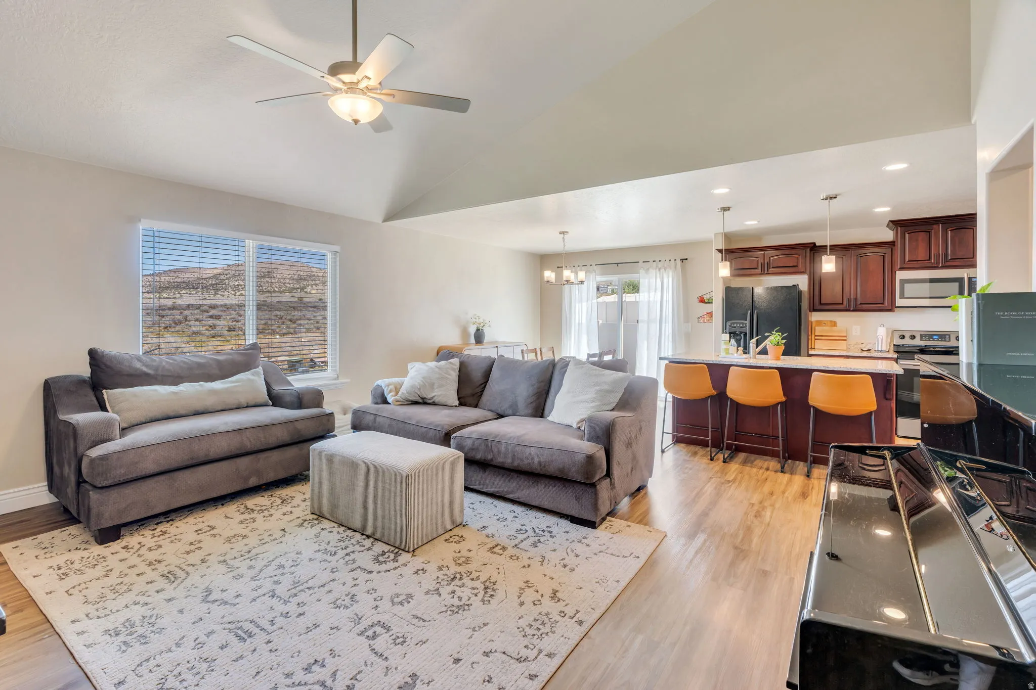 Vaulted ceiling with ceiling fan, wood-finish flooring, kitchen island with seating, dark wood cabinetry, and stainless steel appliances