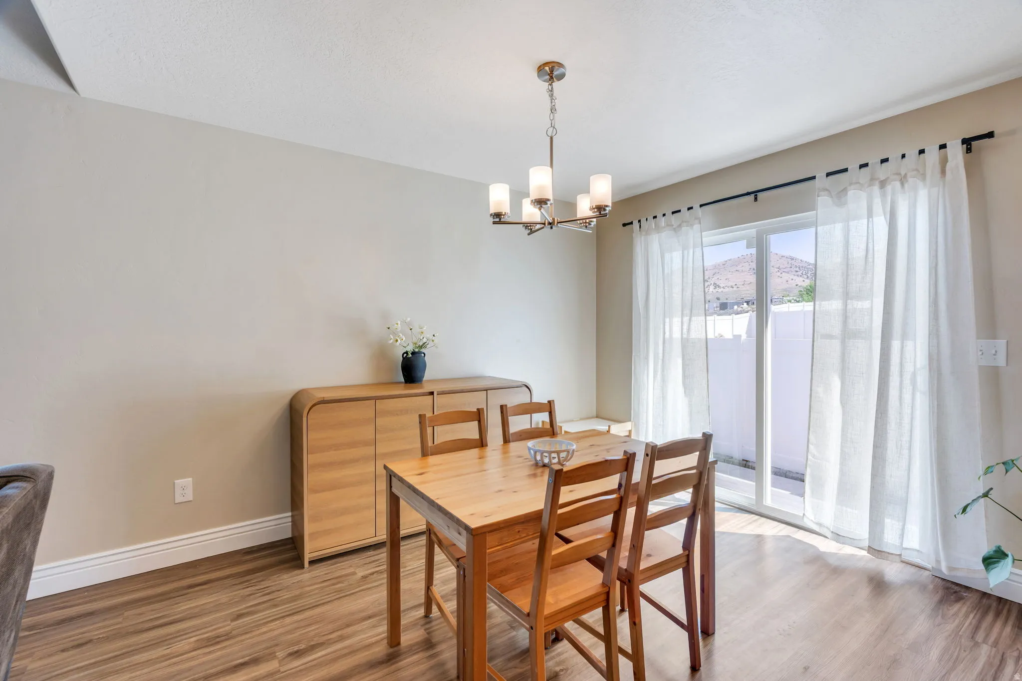Wood-finish flooring, overhead chandelier, light neutral wall paint, and sliding glass door