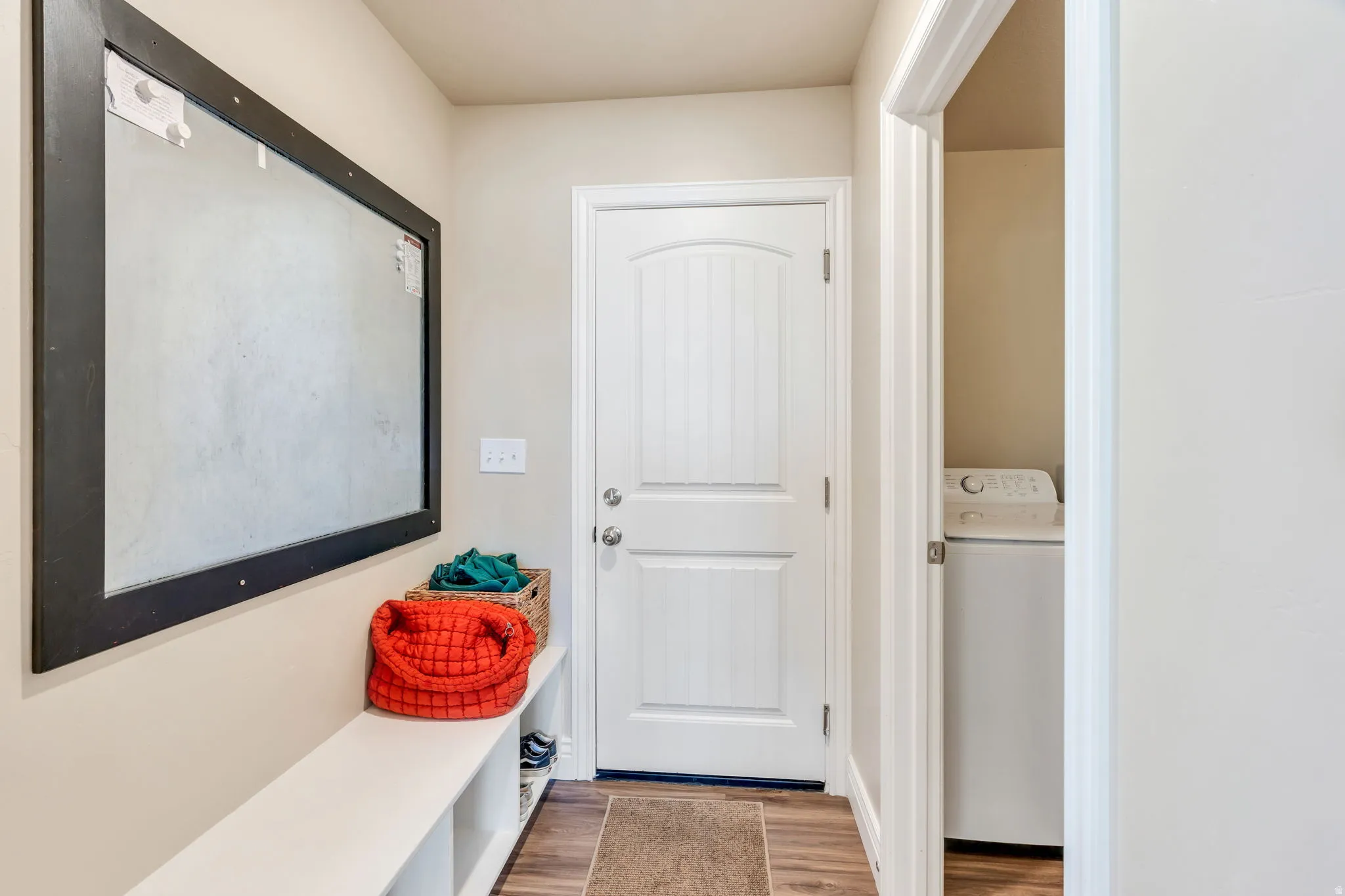Wood-finish flooring, white paneled door, built-in white bench with cubbies, light-colored walls, laundry appliance