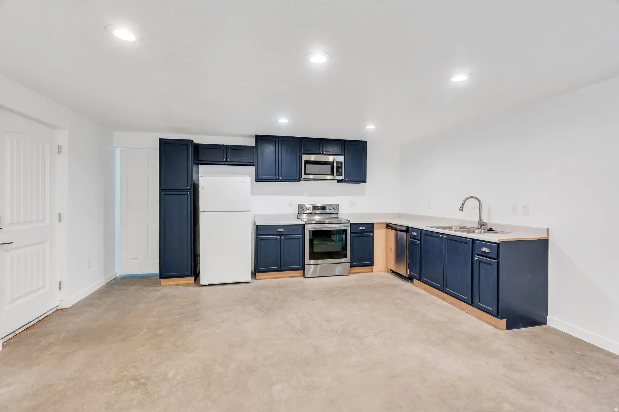 Kitchen featuring dark wood cabinetry, light countertops, stainless steel appliances, and concrete flooring