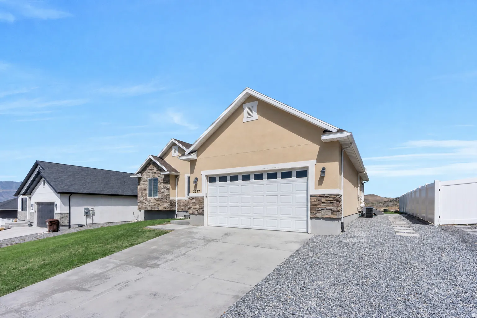 Stucco exterior with stone accents, attached two-car garage, concrete driveway, and gravel landscaping