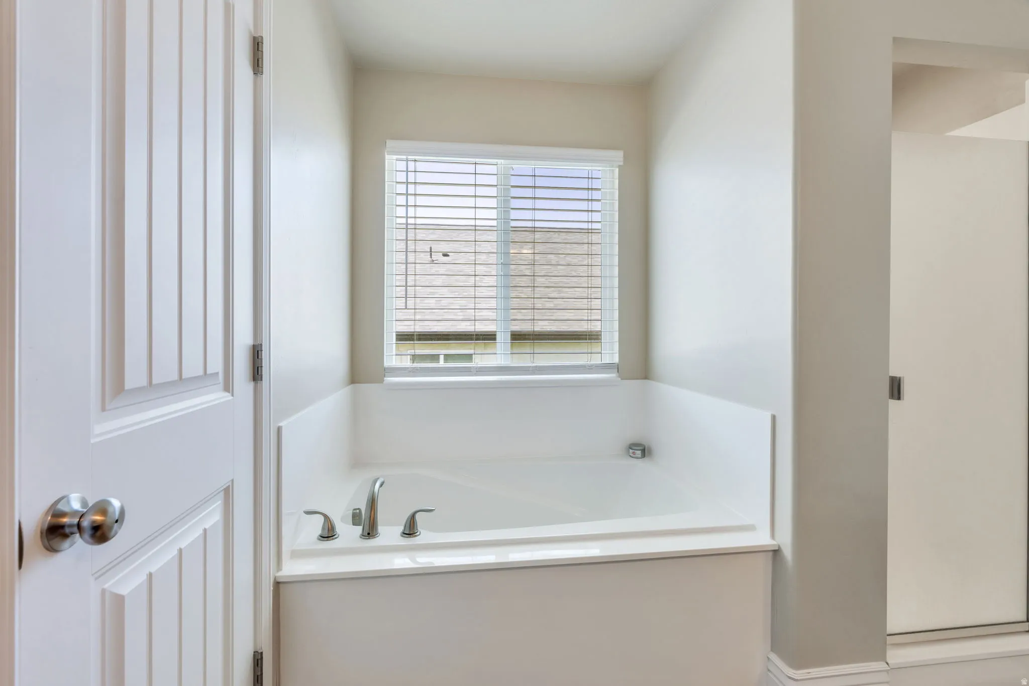 Built-in soaking tub with deck-mounted fixtures, adjacent to a window with blinds