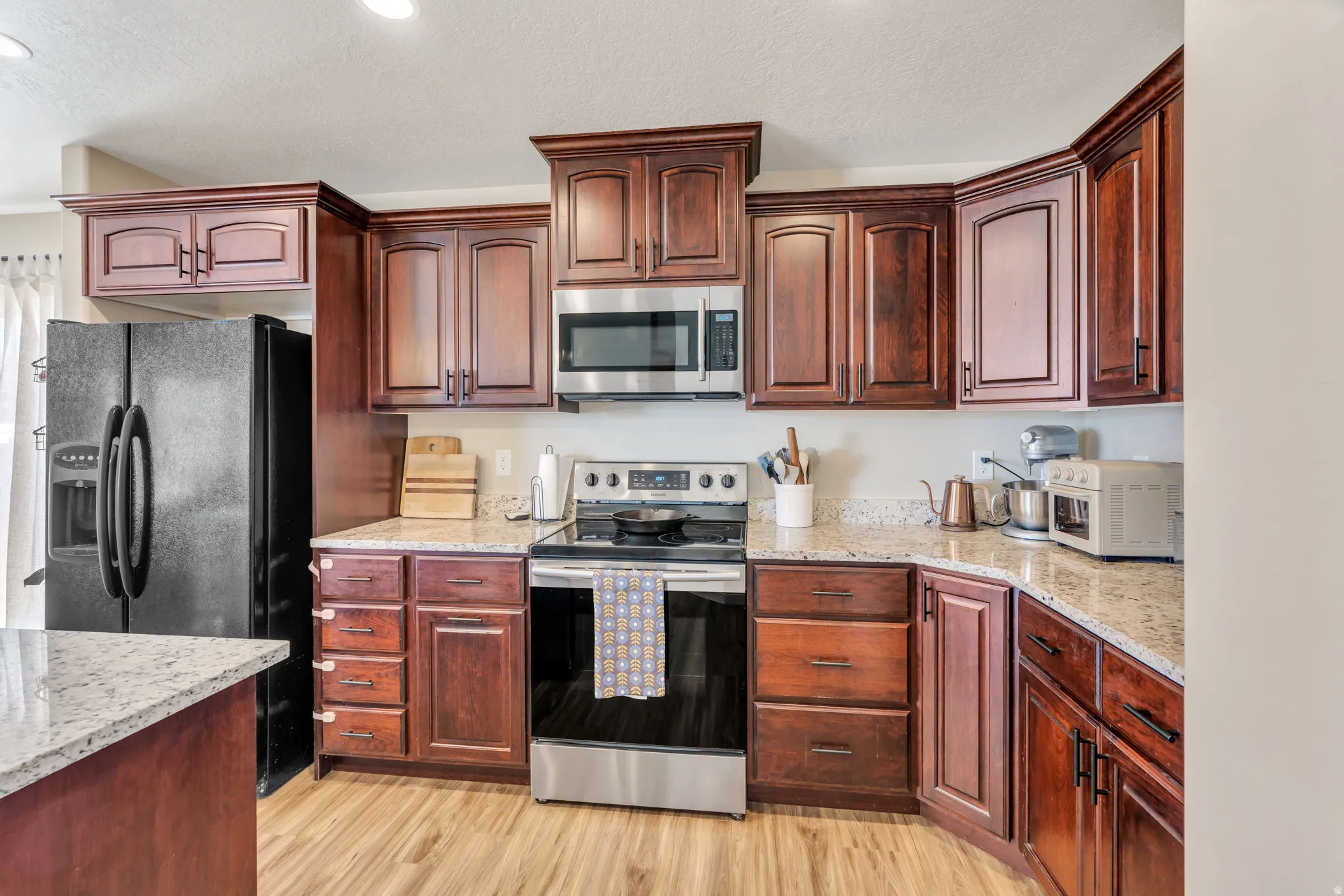 Kitchen featuring wood-finish flooring, wood cabinetry, stone countertops, and stainless steel appliances