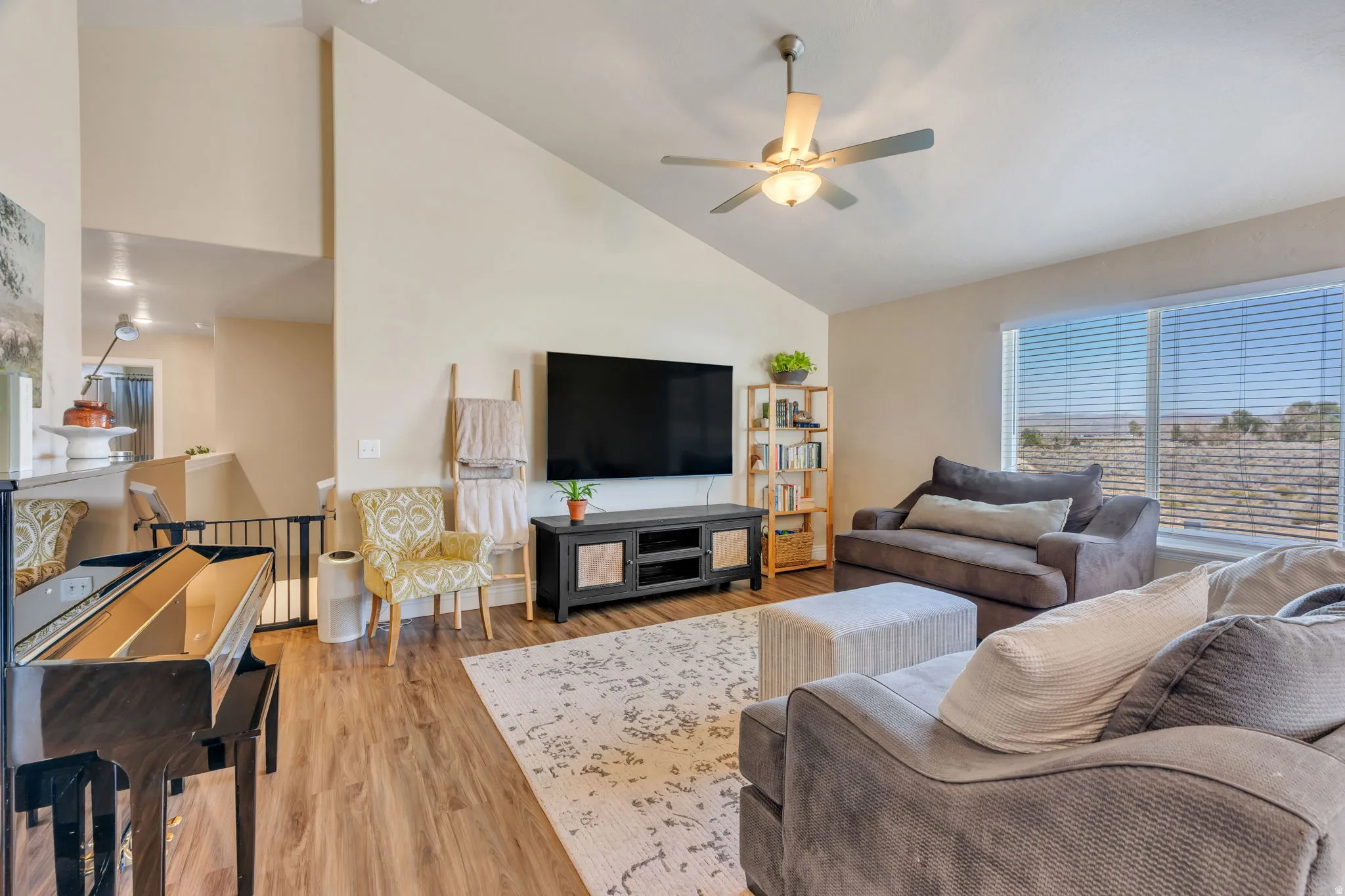Vaulted ceiling with a ceiling fan, wood-finish flooring, and large windows