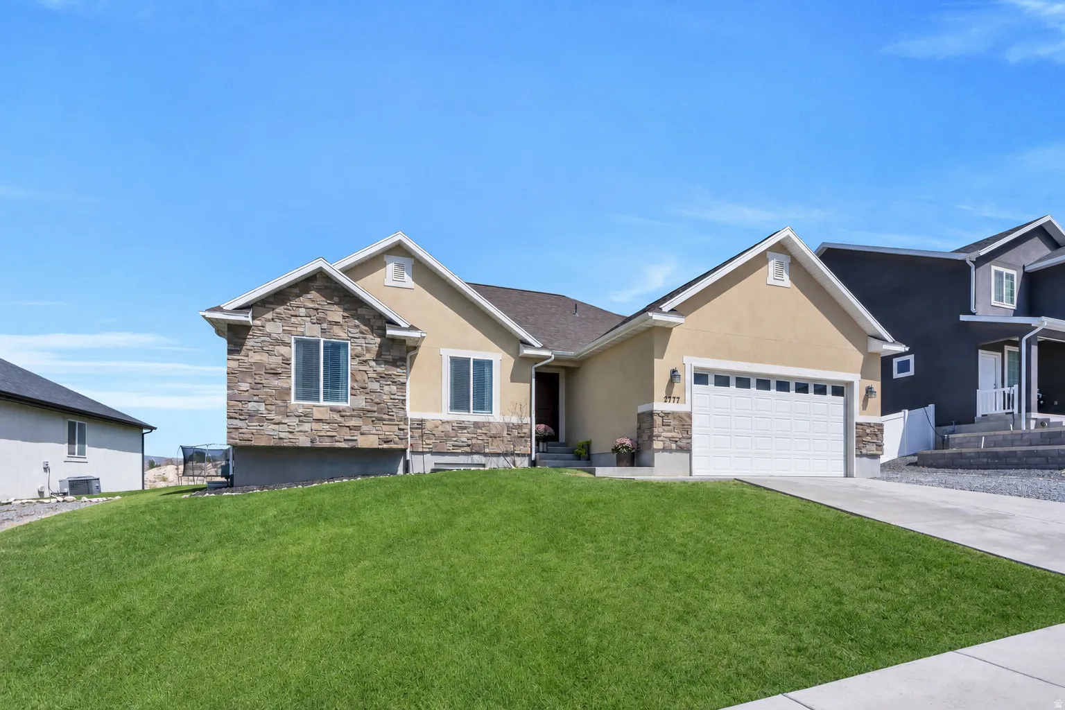 Stucco and stone facade with multiple gables, an attached garage, and a concrete driveway