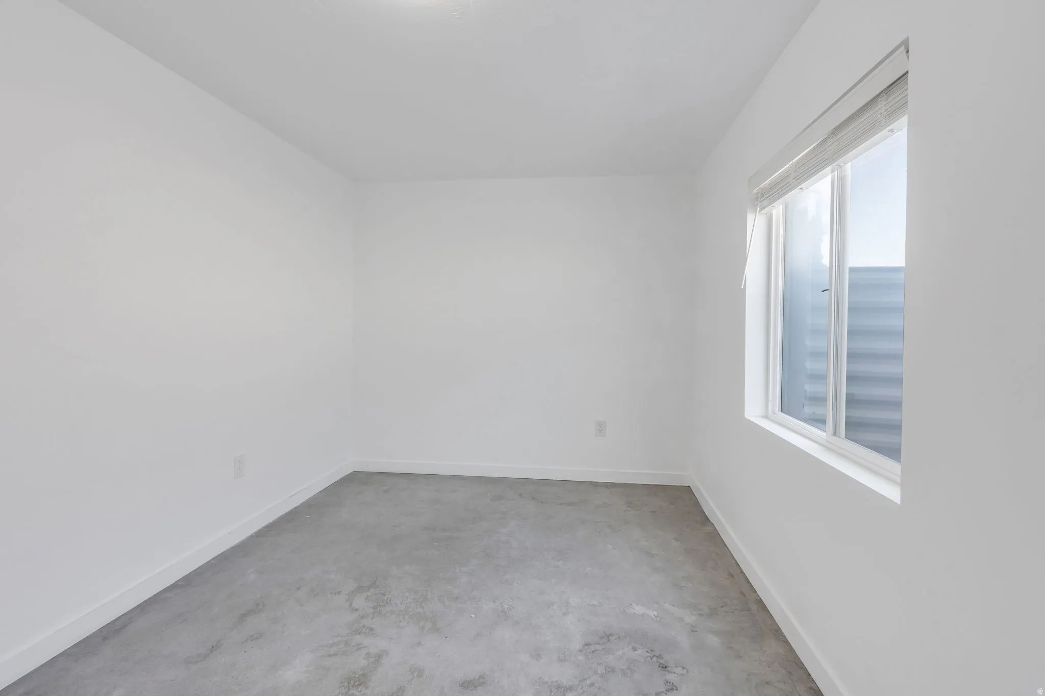 Recessed lighting fixture, bright white walls, white trim, window with blinds, and concrete flooring