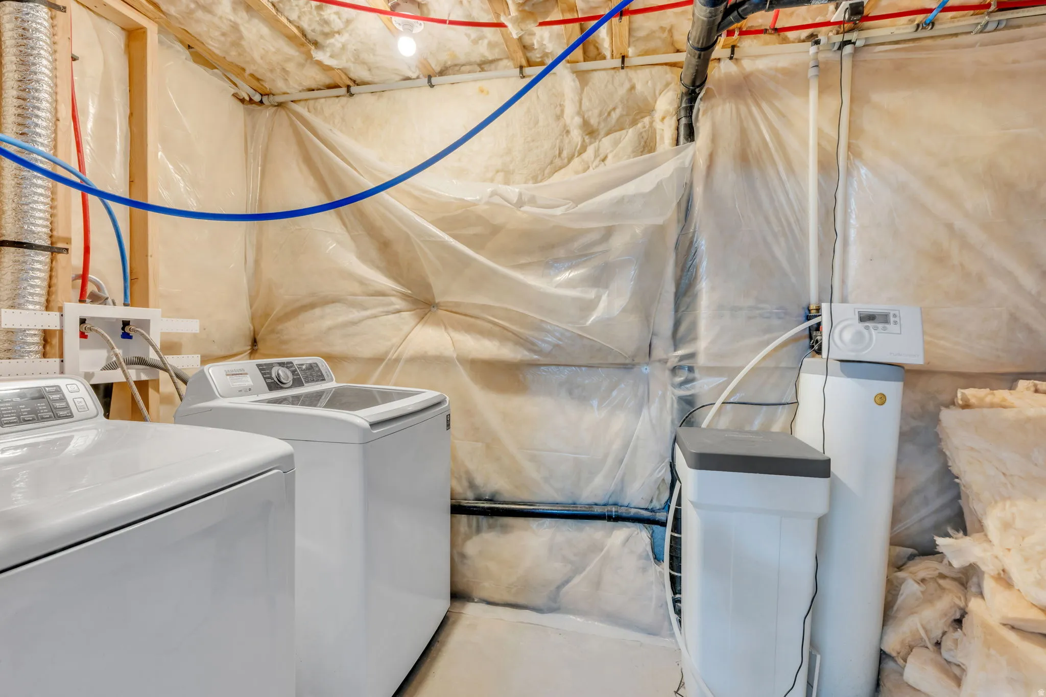 Dedicated laundry area featuring a washer and dryer, exposed ceiling joists, and a water softener system