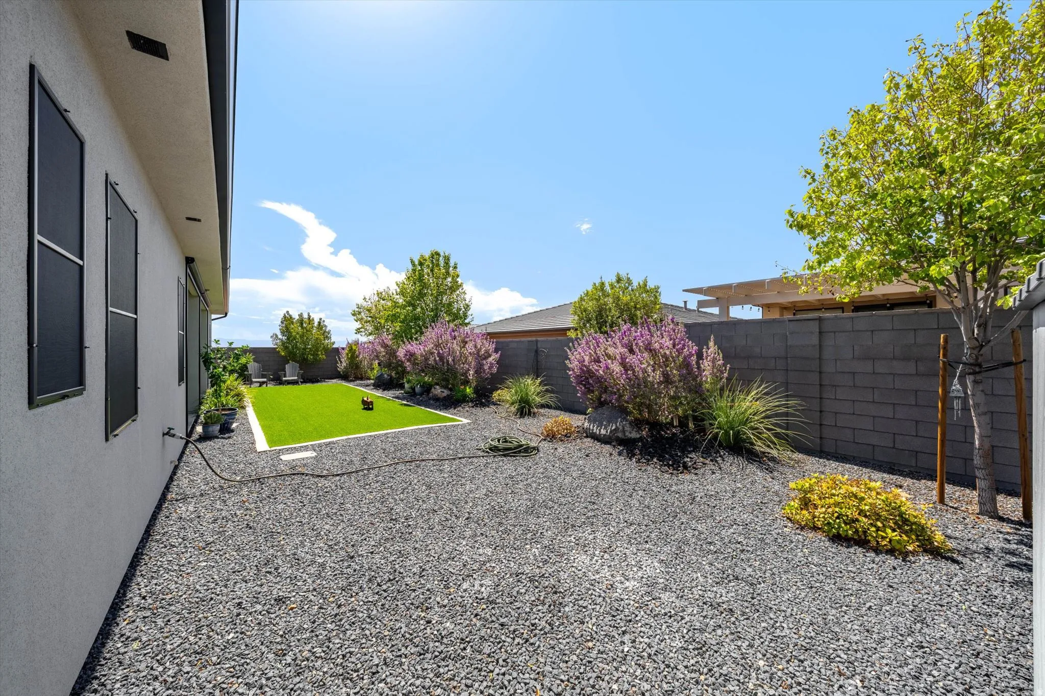 Landscaped backyard featuring decorative gravel, a central synthetic lawn, mature trees, and a block perimeter fence