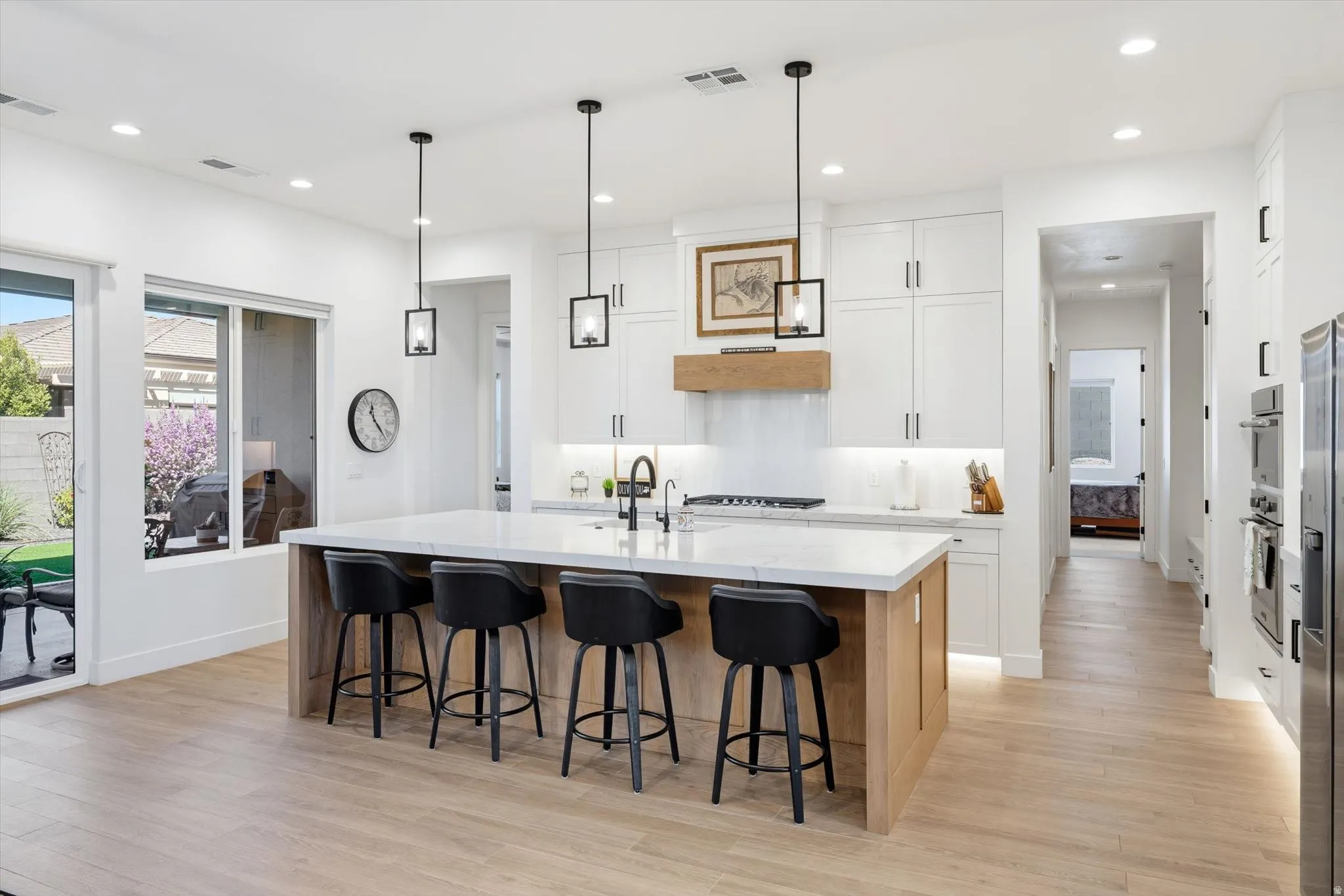 Kitchen featuring a spacious island with seating, pendant lighting, built-in appliances, white cabinetry, and wood-finish flooring