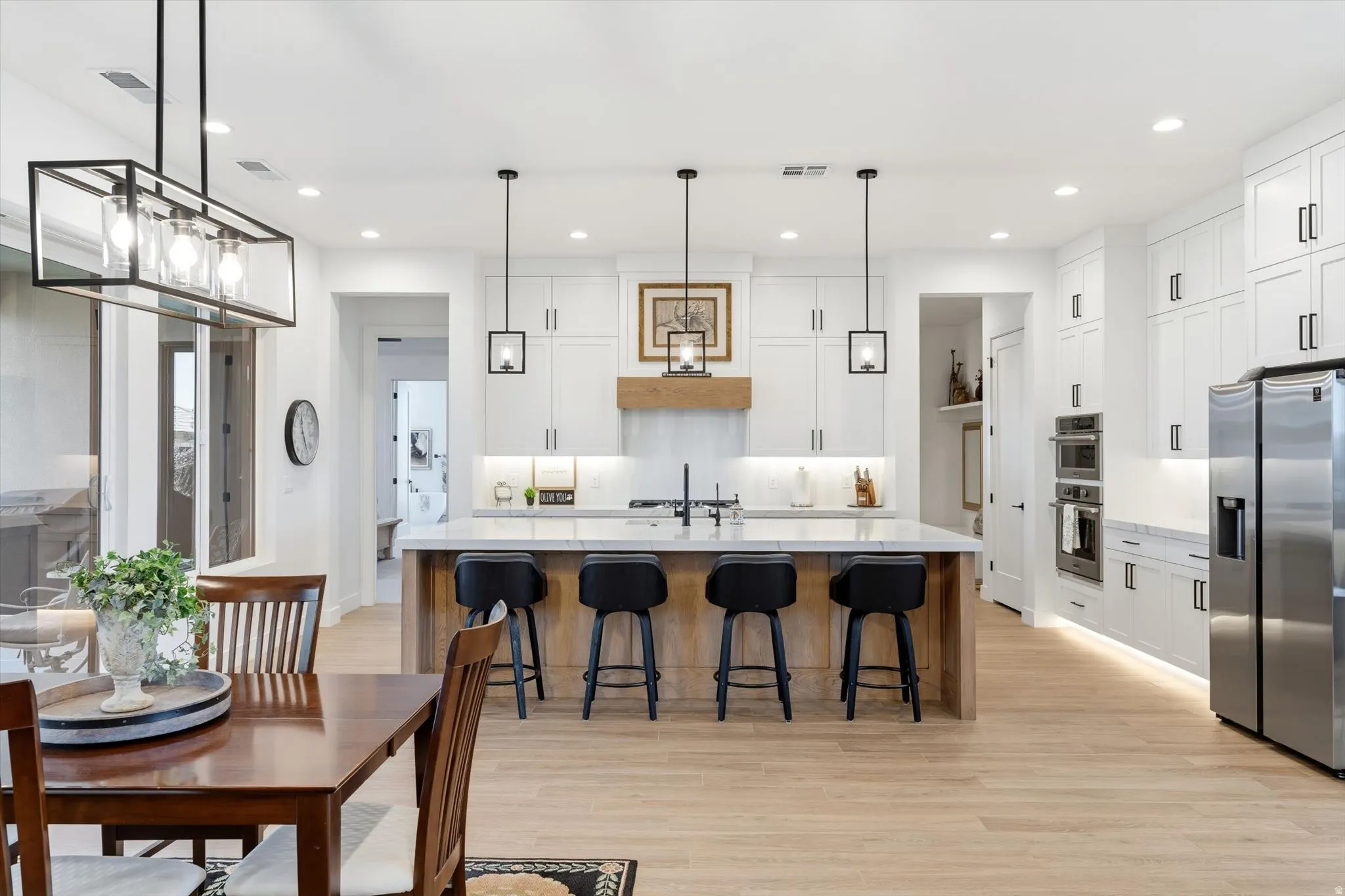 Spacious kitchen featuring an expansive center island, white cabinetry, stainless steel appliances, wood-finish flooring, and recessed lighting