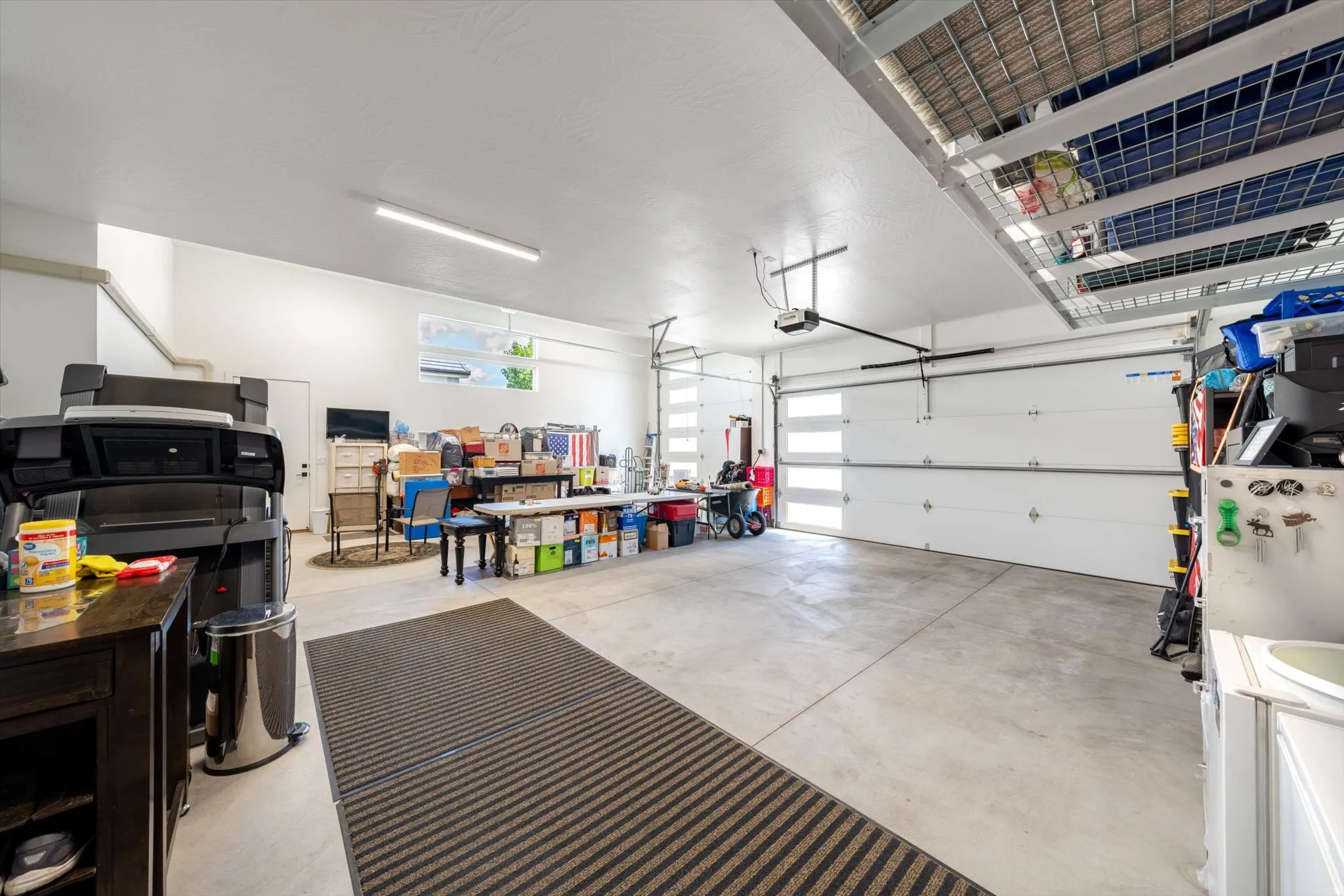 Spacious garage featuring concrete flooring, overhead storage racks, dual garage doors with frosted glass panels, and a utility sink
