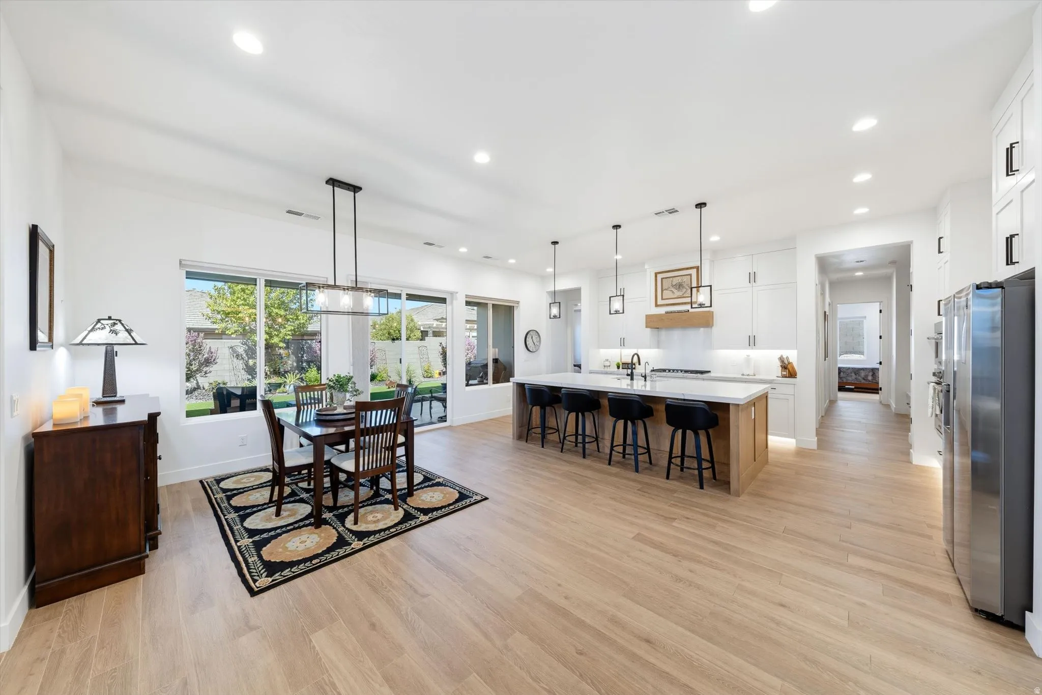 Expansive open-concept space featuring wood-finish flooring, white cabinetry, a large kitchen island with pendant lighting, and recessed ceiling lights