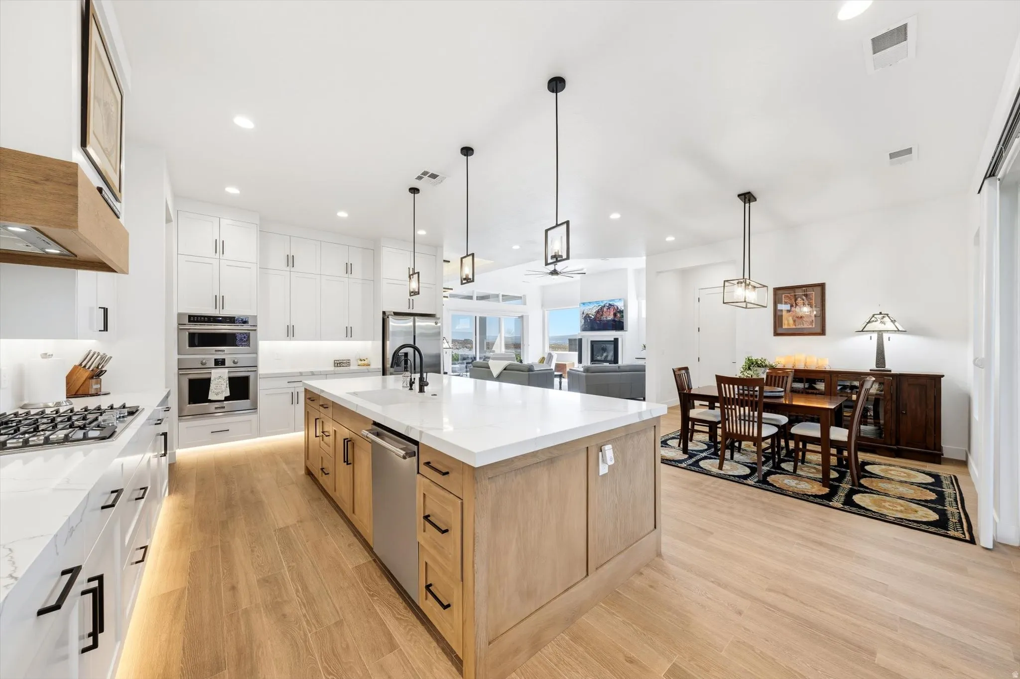 Gourmet kitchen with a large central island, white shaker cabinetry, stainless steel appliances, and wood-finish flooring