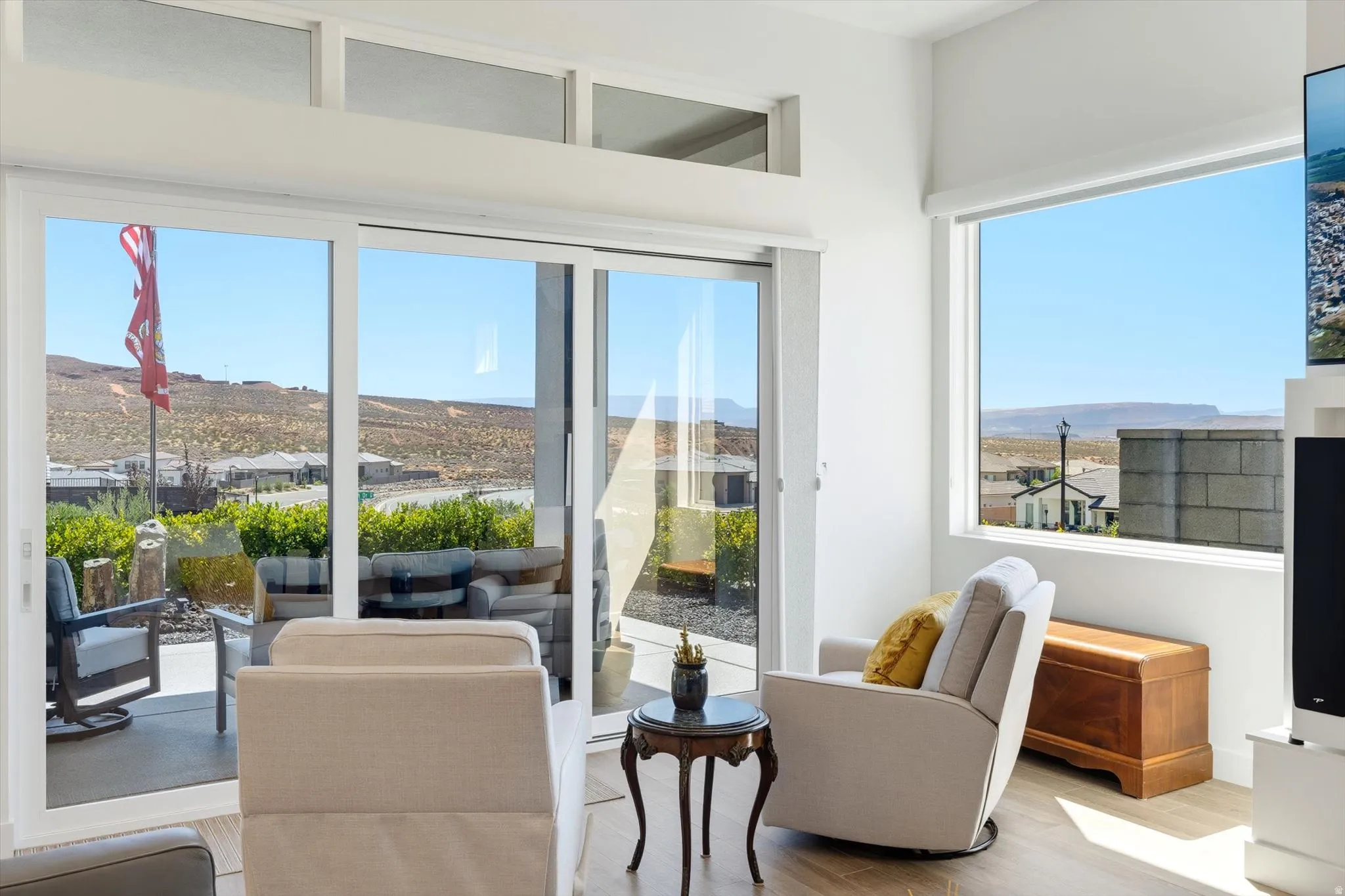 Sliding glass door opening to an outdoor patio with a mountain backdrop, complemented by a large picture window, high ceilings, and light wood-finish flooring