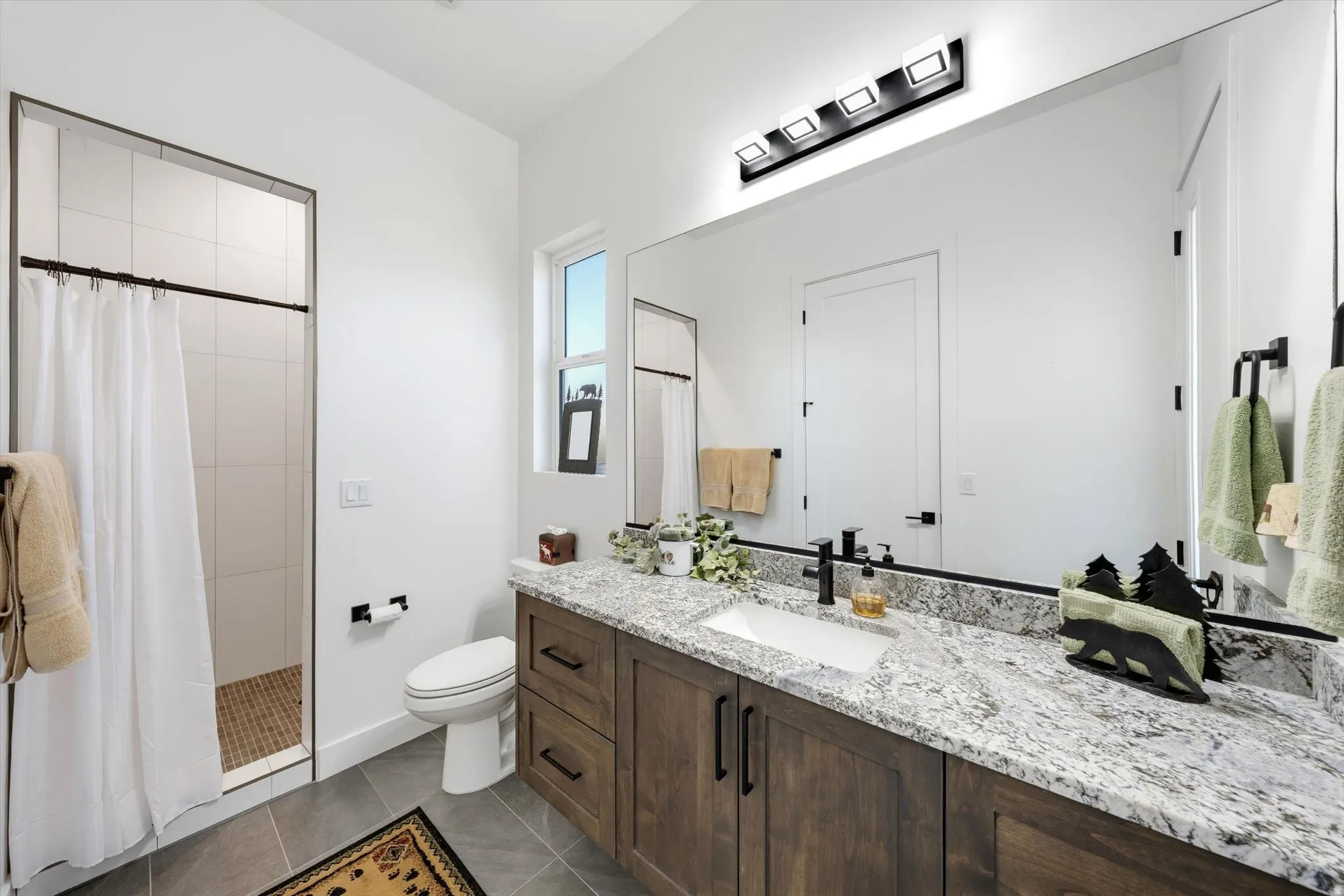 Spacious bathroom featuring a wood-finish vanity with an integrated sink, broad mirror, and a tiled shower with a pebble-finish floor