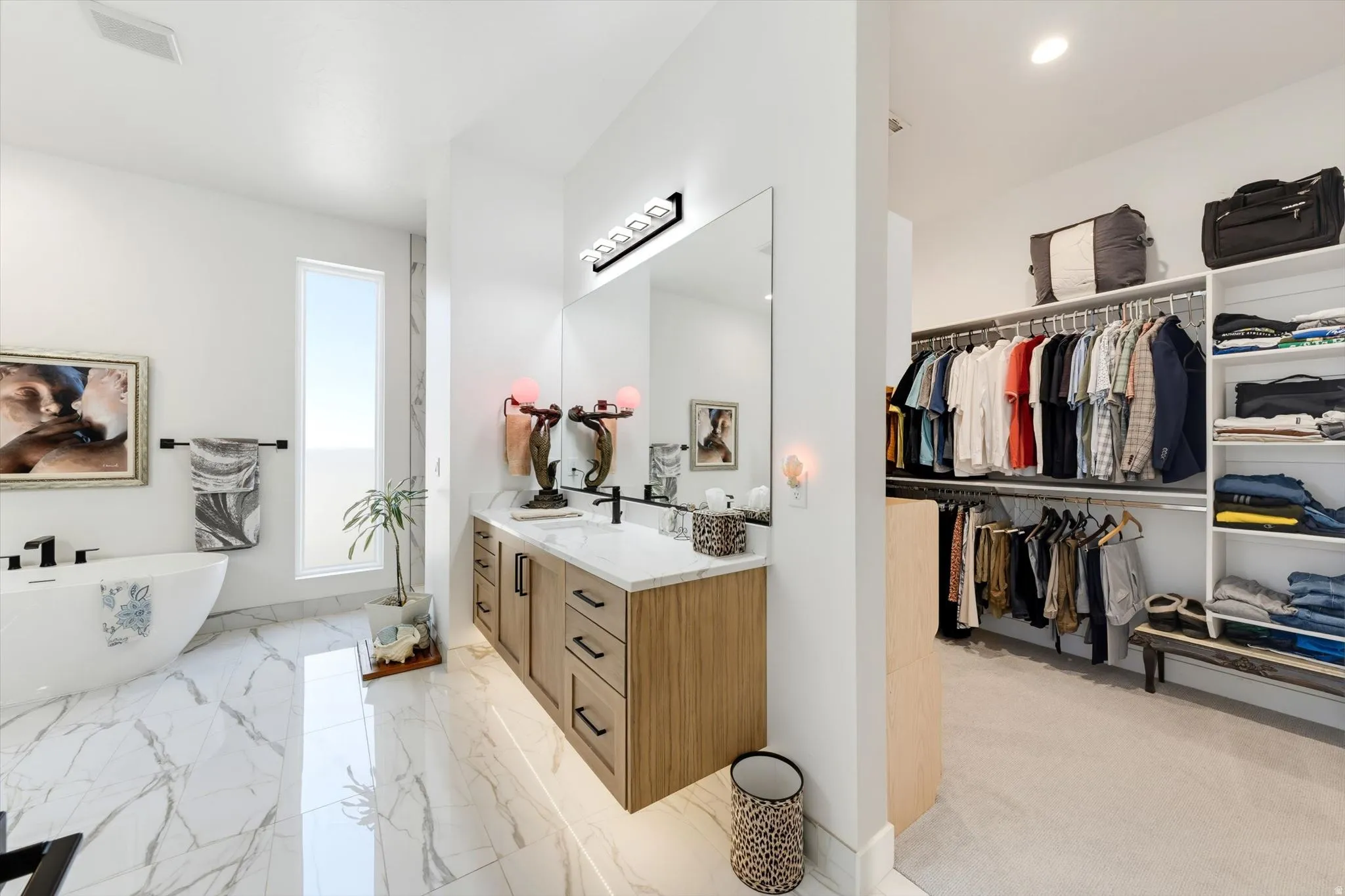 Freestanding soaking tub, wood-finish double vanity with stone countertop, large wall mirror, and walk-in closet with built-in shelving