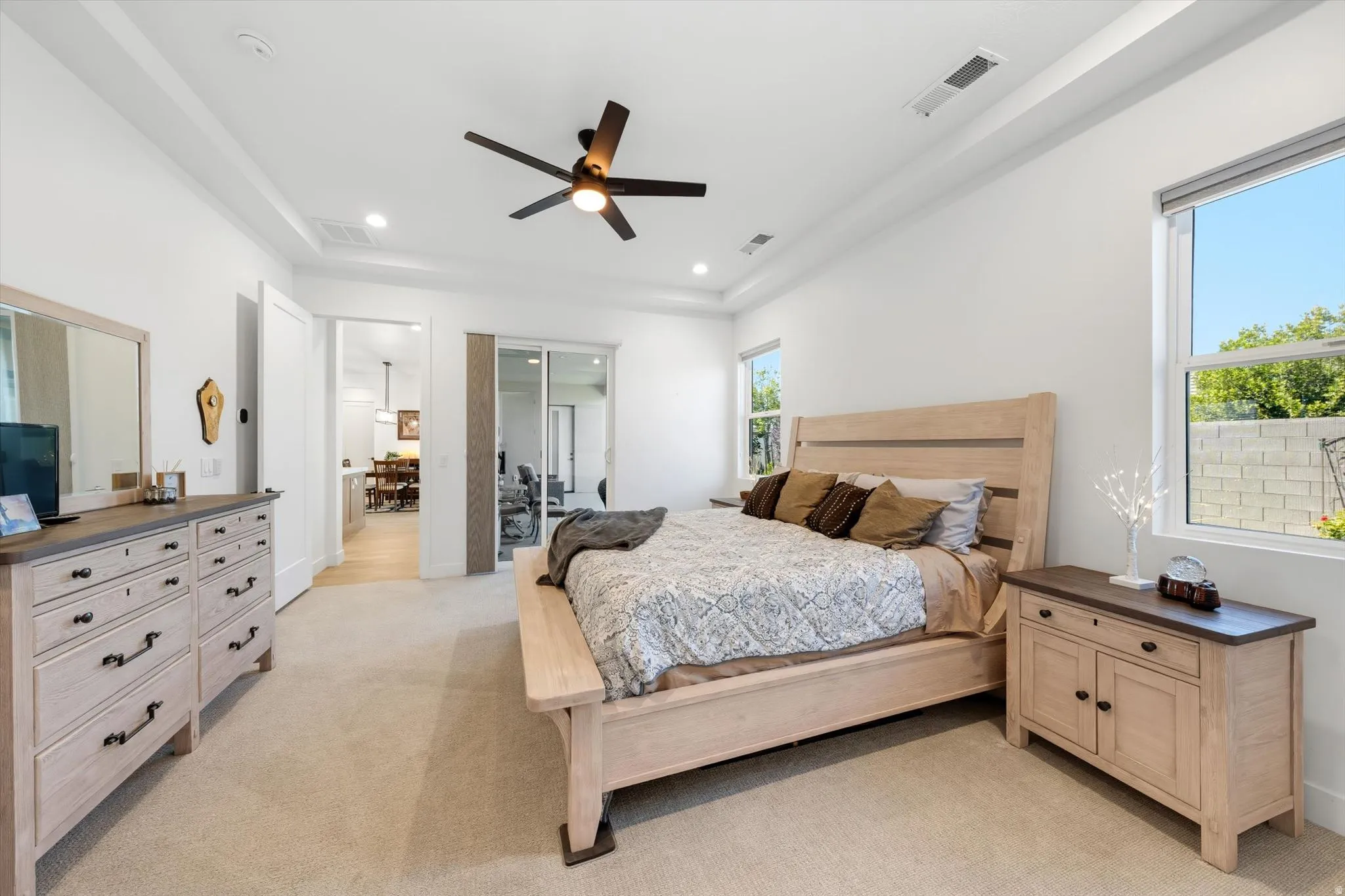 Tray ceiling with recessed lighting, ceiling fan, carpet flooring, dual windows, and an interior sliding door