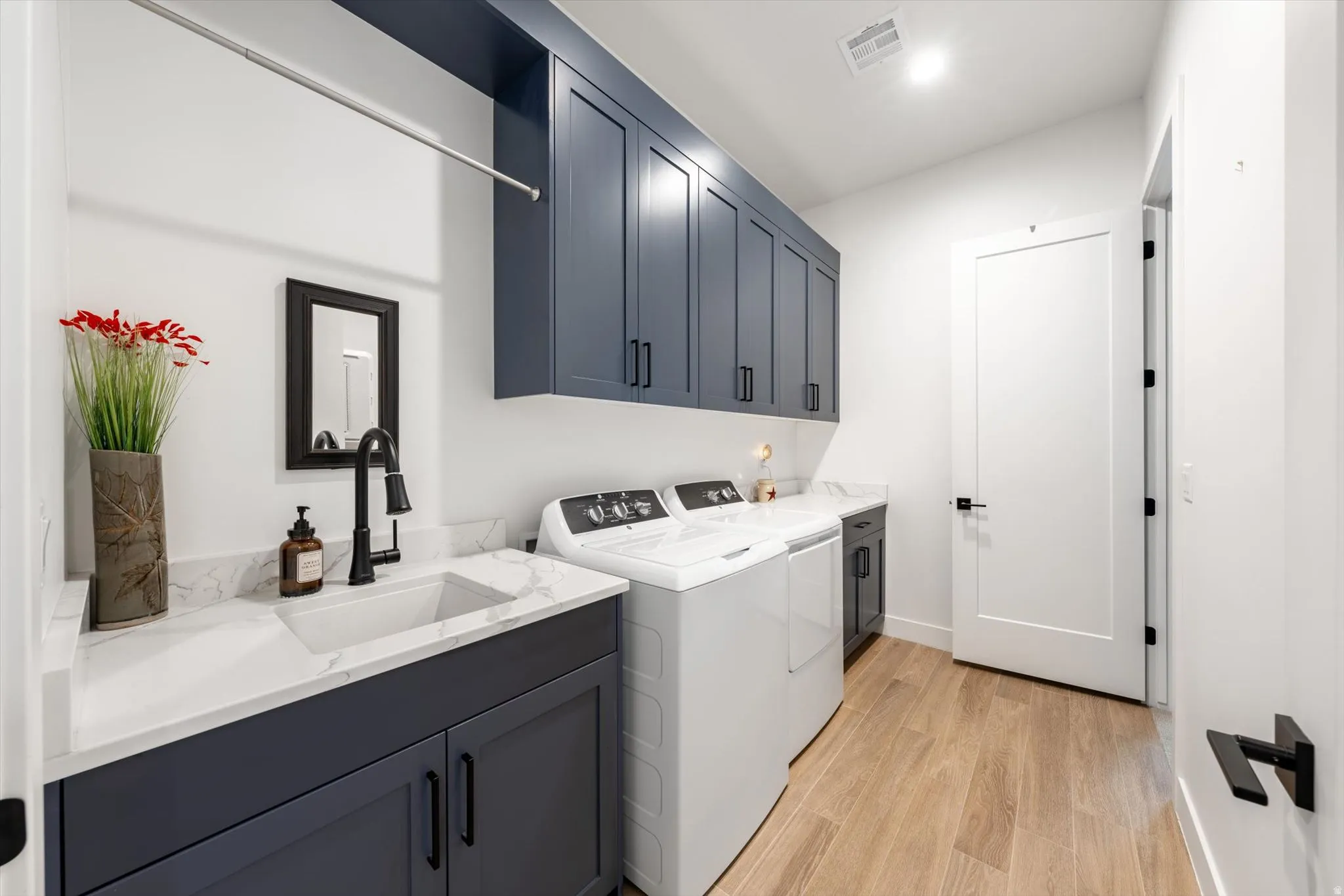 Laundry room featuring wood-finish flooring, built-in cabinetry, an undermount sink, and stone-finish countertops