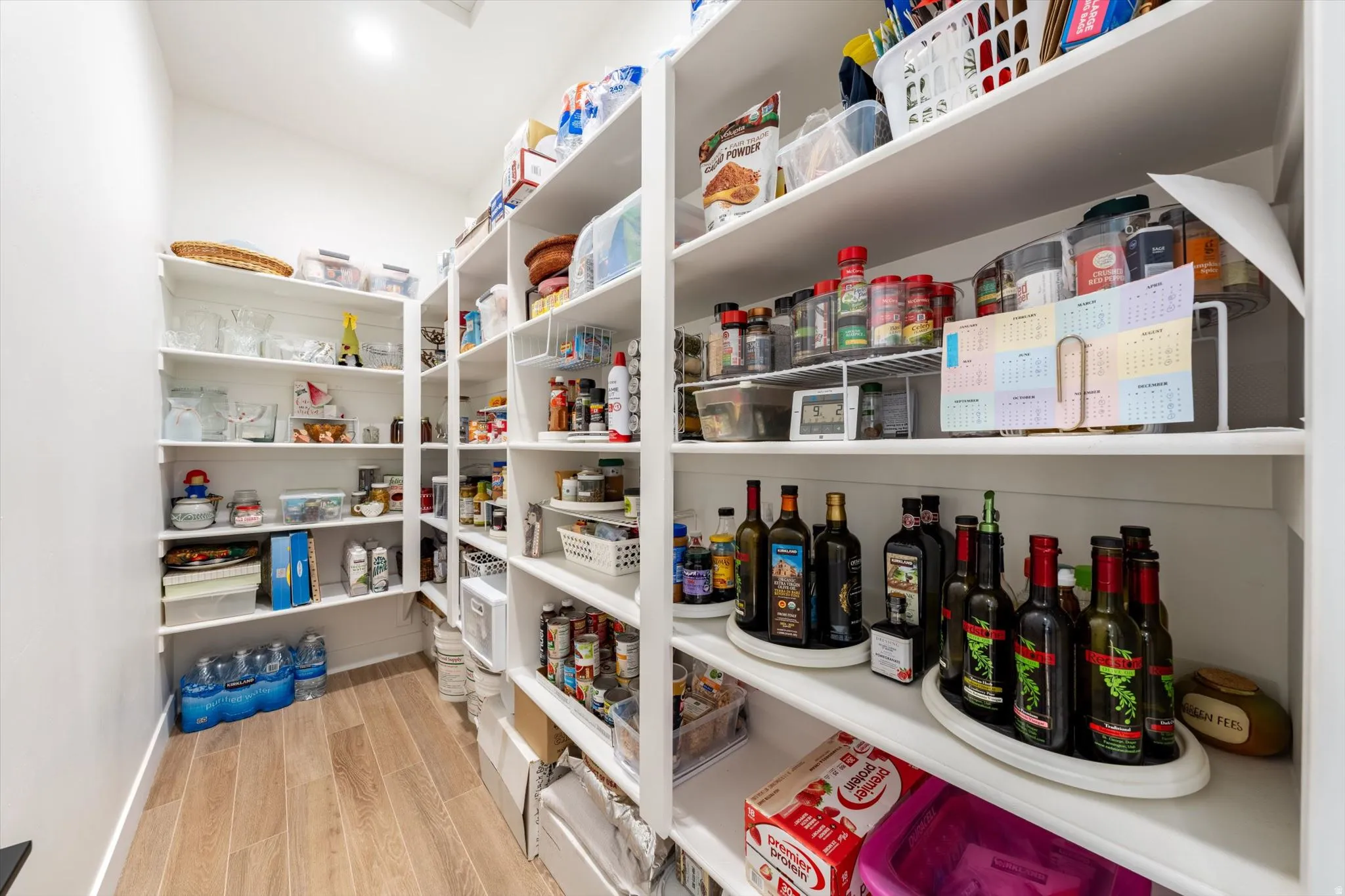 Spacious walk-in pantry with extensive built-in shelving, wood-finish flooring, and recessed overhead lighting