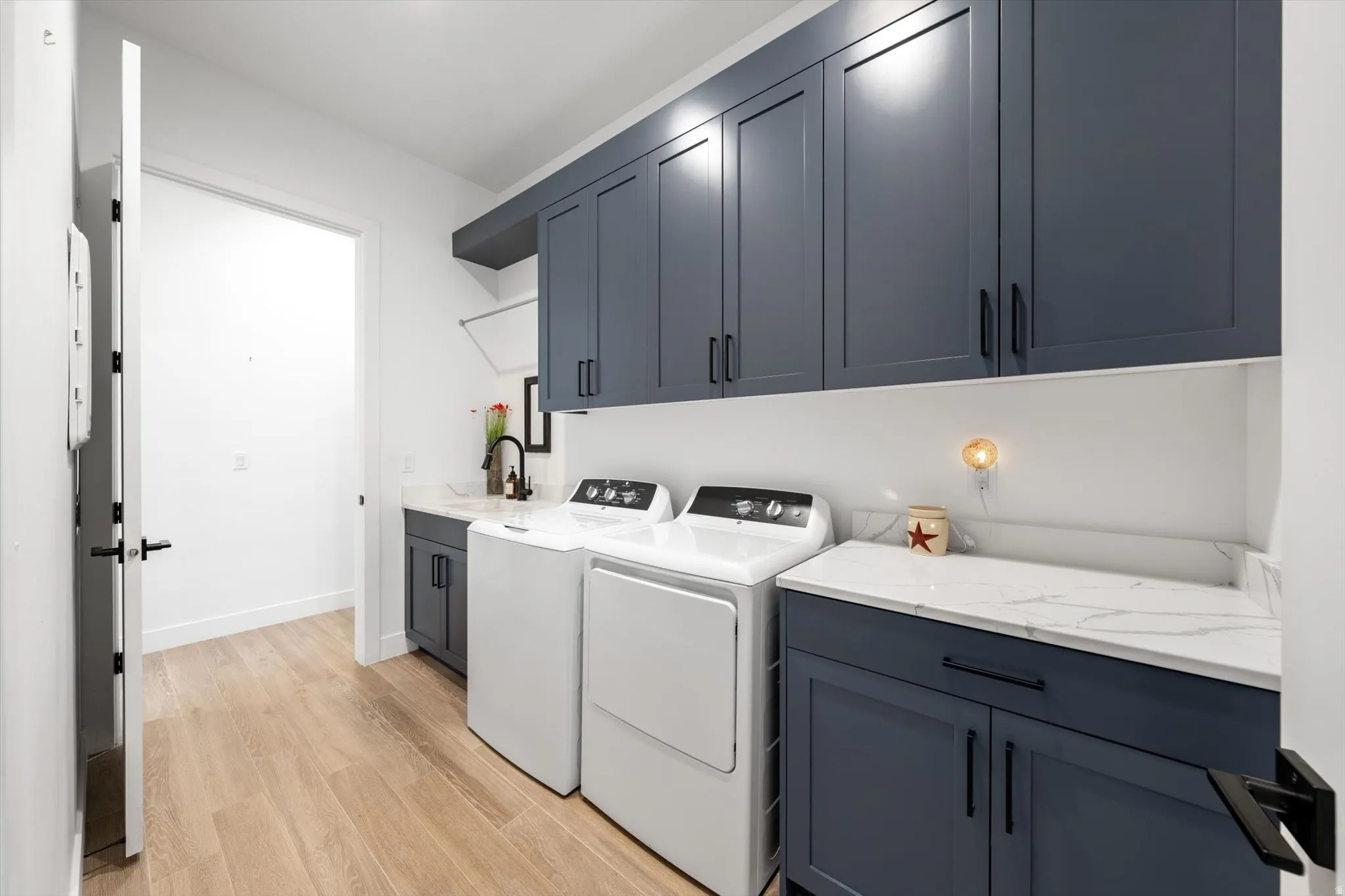 Laundry area featuring wood-finish flooring, white walls, and dark blue cabinetry with black hardware