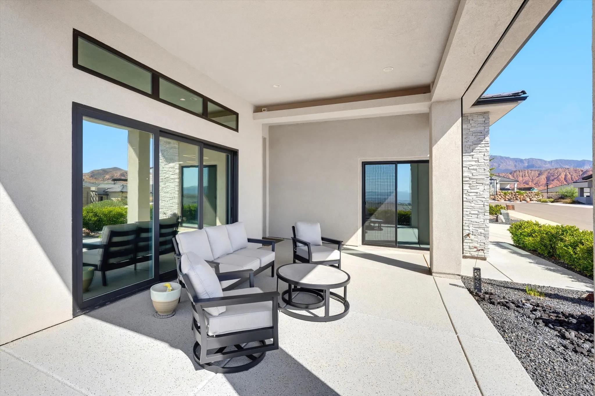 Covered patio with a concrete surface, stone veneer columns, and dark-framed sliding glass doors
