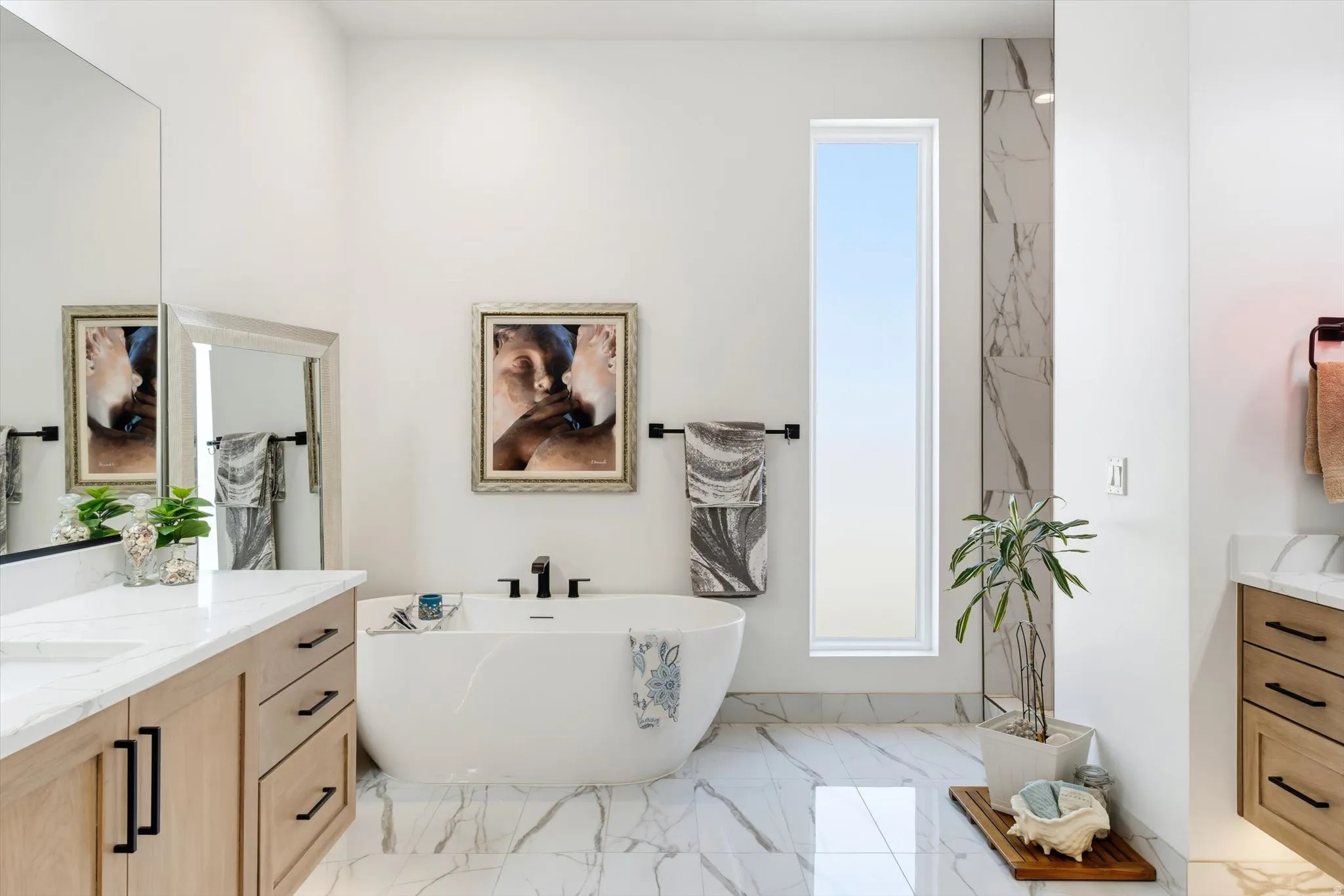 Freestanding soaking tub, dual floating vanities with quartz countertops, marble-finish flooring, and a vertical window