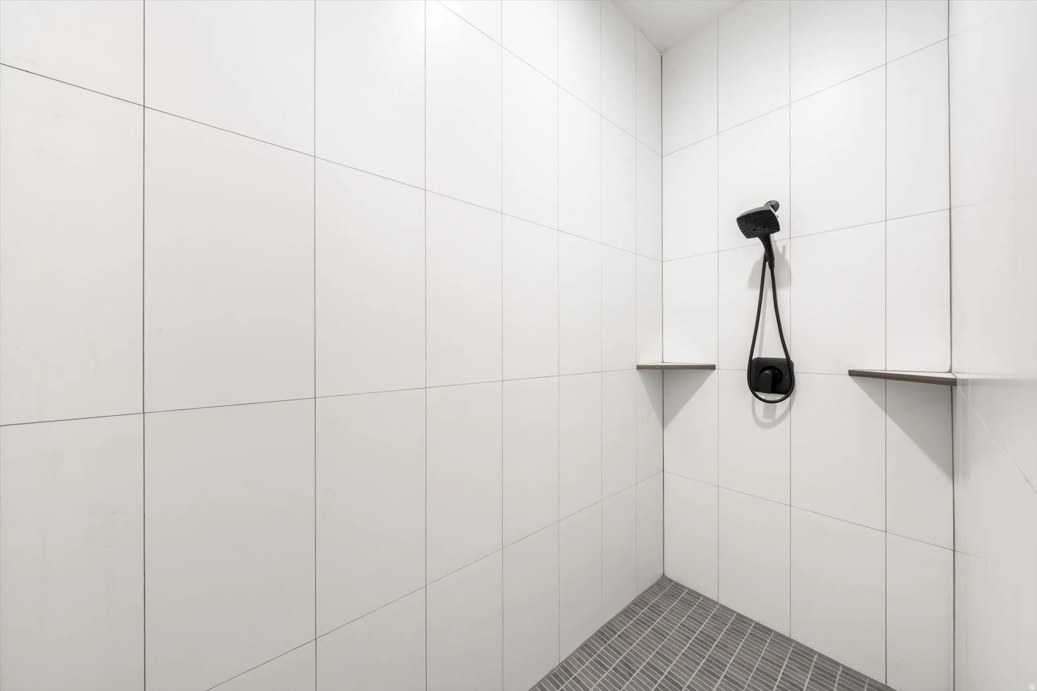 White tiled shower enclosure with a matte black shower head and control, complemented by two built-in corner shelves