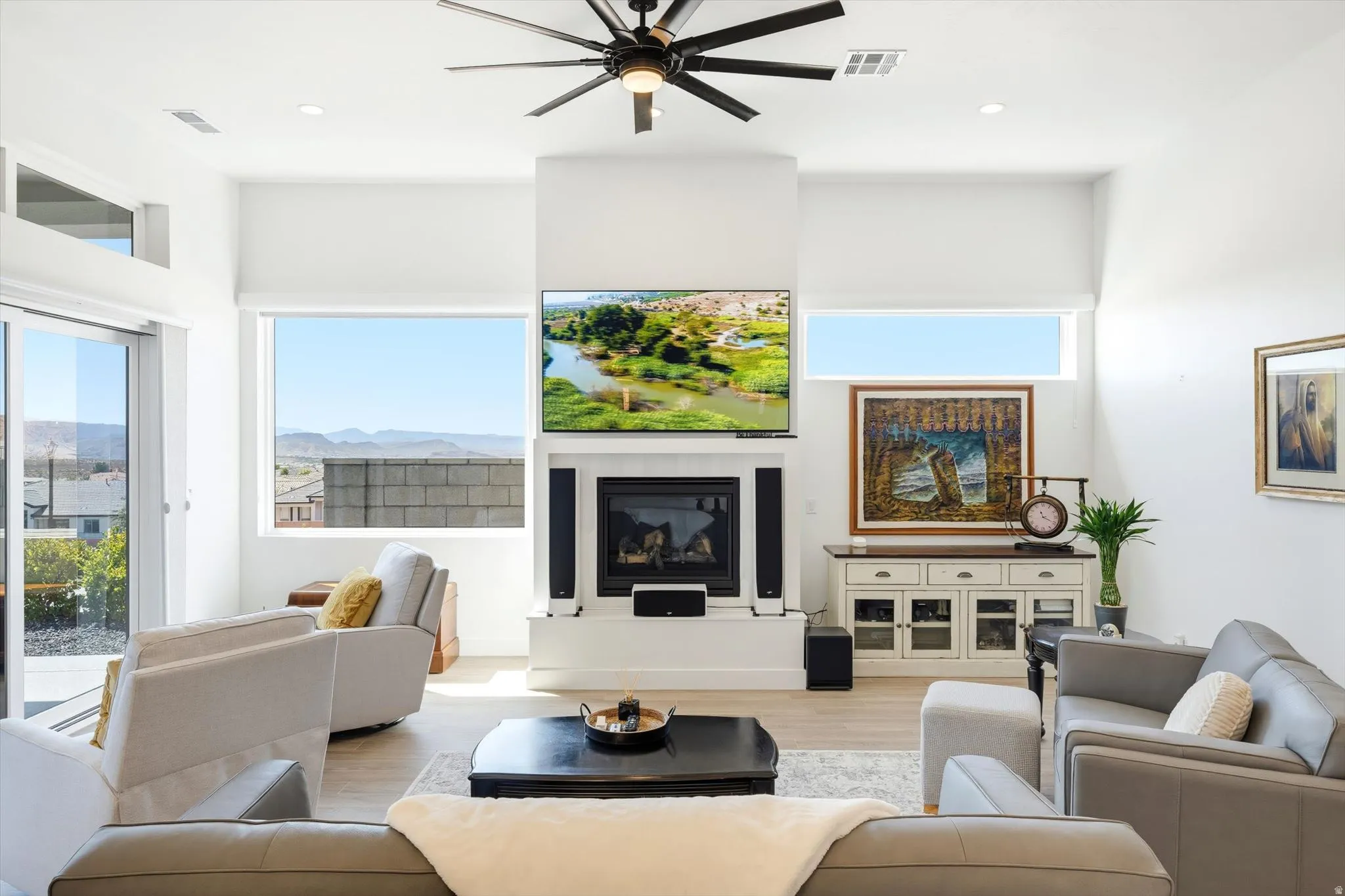 Living area featuring a fireplace, a ceiling fan, light wood-finish flooring, and expansive windows