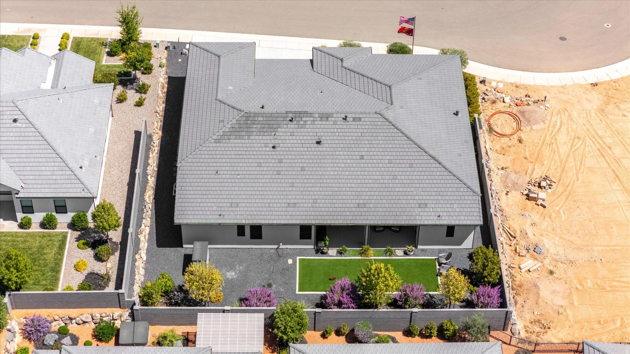Gray tiled roof, covered patio, artificial turf, perimeter fencing, and established landscaping
