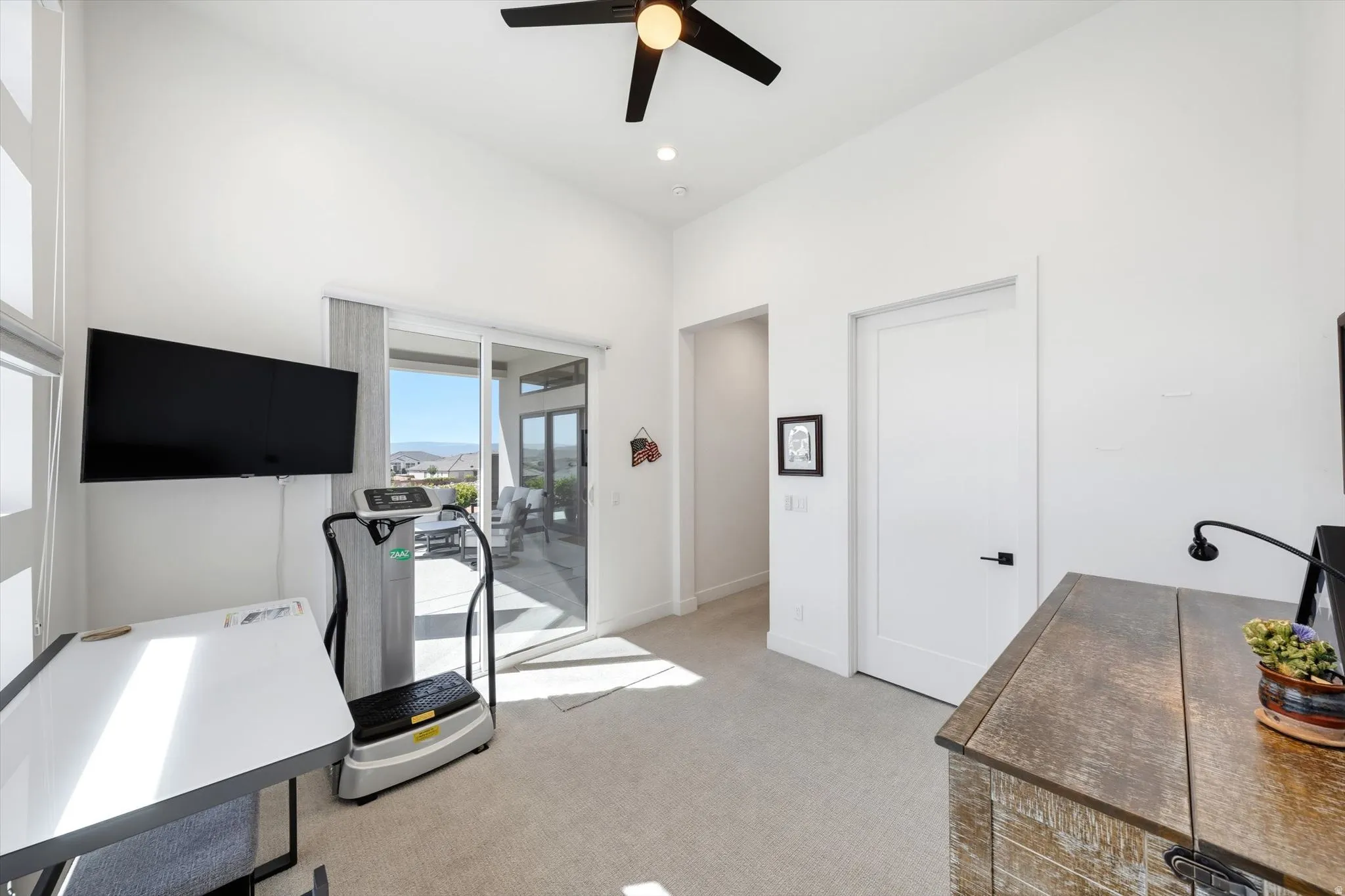 White walls with vaulted ceiling, ceiling fan with light fixture, light gray carpet, and sliding glass doors to outdoor patio