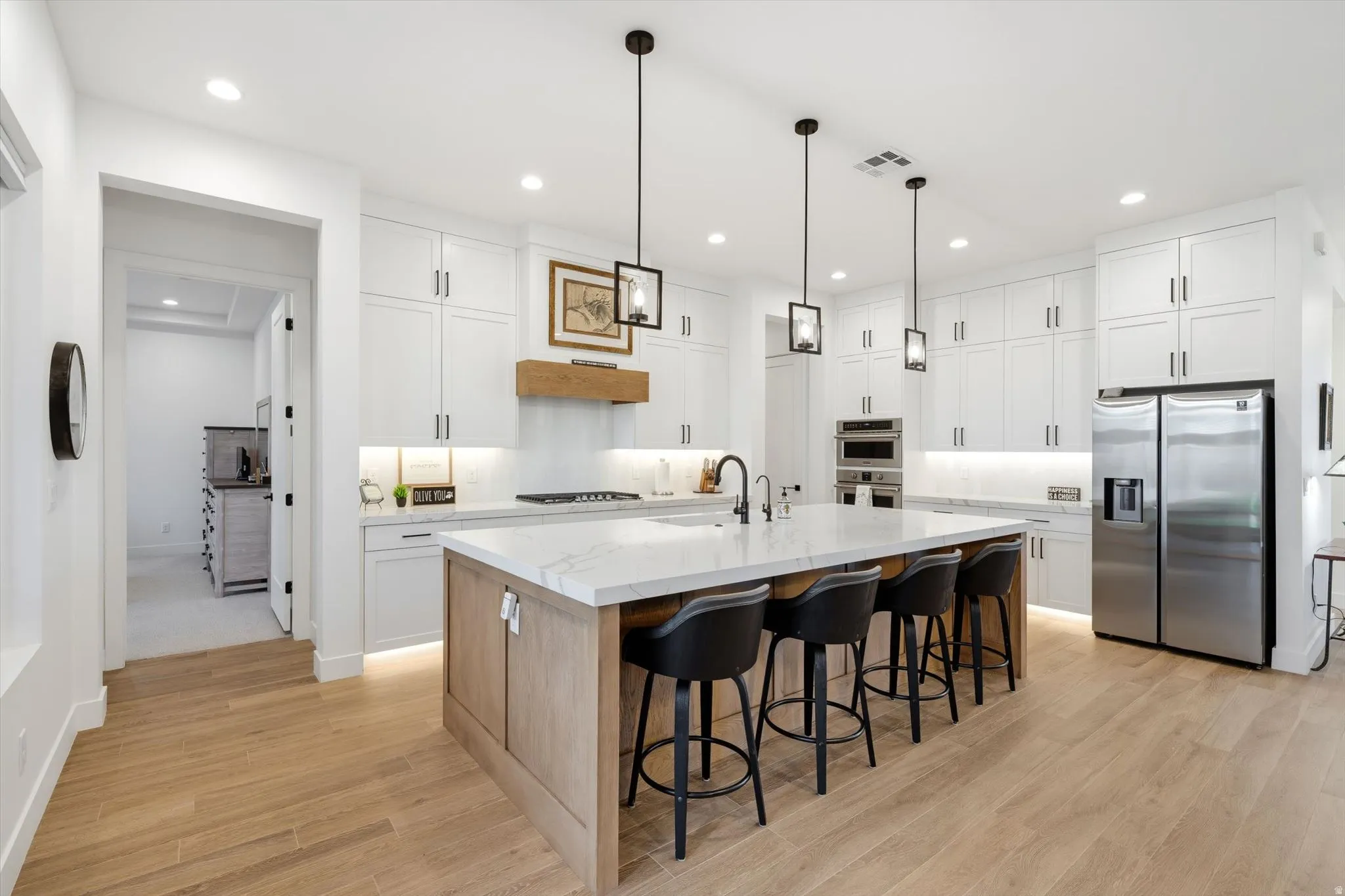 Spacious kitchen featuring white cabinetry, a large center island with seating, stainless steel appliances, and wood-finish flooring