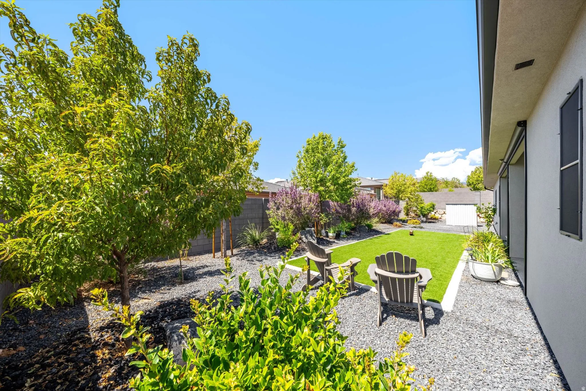 Landscaped backyard featuring artificial turf, decorative gravel, and mature trees