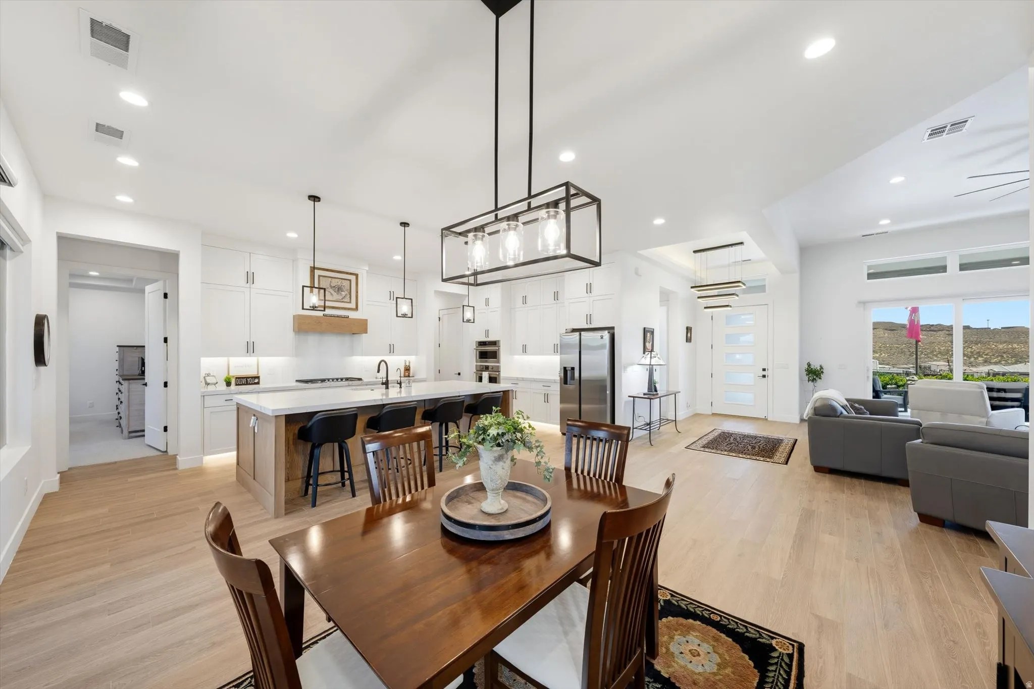 Open-concept living space featuring wood-finish flooring, white cabinetry, a large kitchen island with seating, a built-in stainless steel refrigerator, and recessed lighting