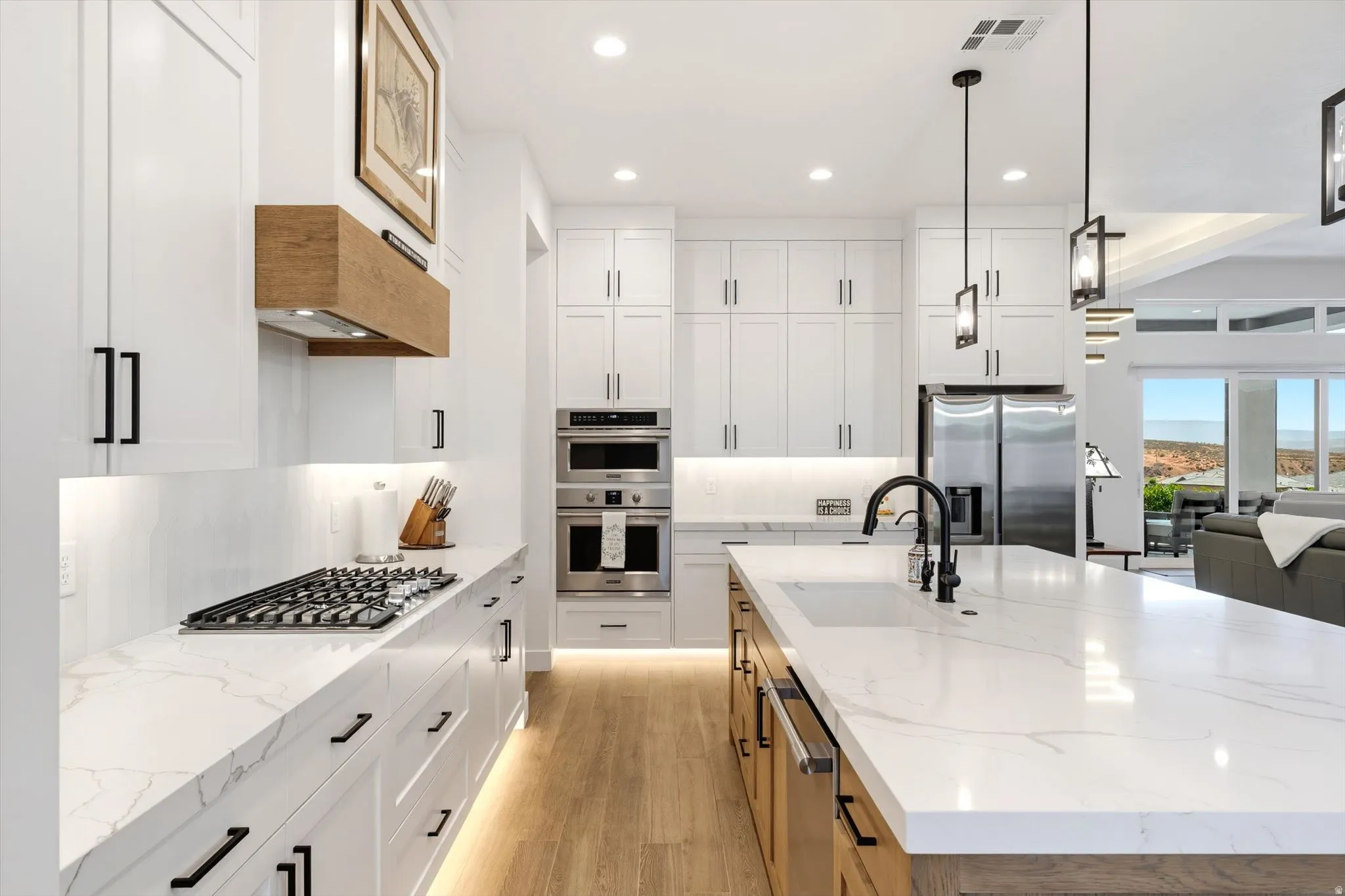 White shaker cabinetry with black hardware, stainless steel appliances, solid surface countertops, a center island with sink, and wood-finish flooring