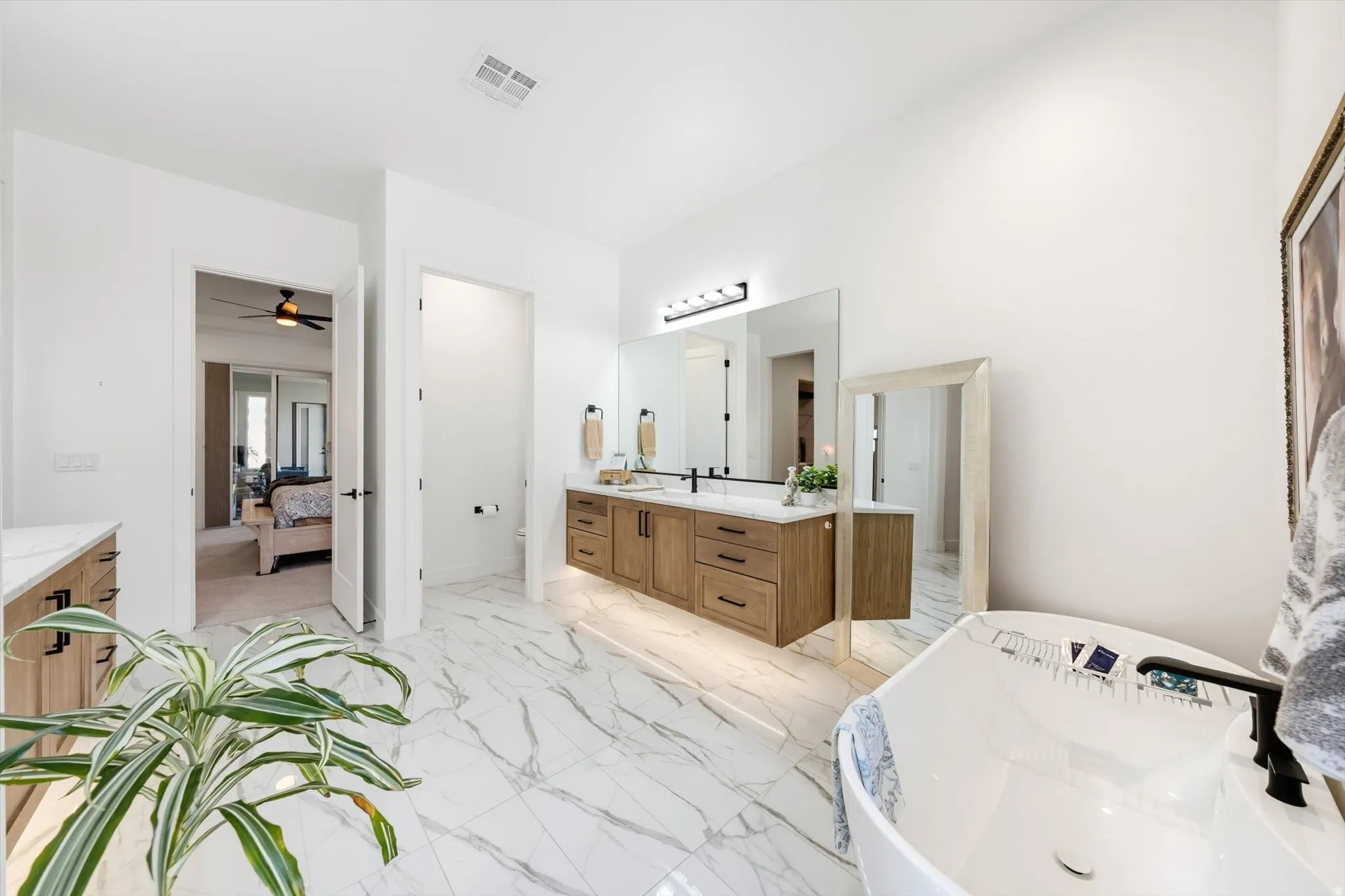 White marble-look flooring, freestanding soaking tub, wood-finish double vanity, dual mirrors, and contemporary lighting fixture