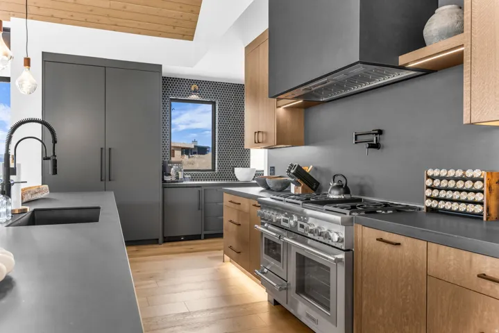 Modern kitchen featuring a wood-finish vaulted ceiling, stainless steel range with a built-in hood, flat-panel cabinetry, and dark countertops