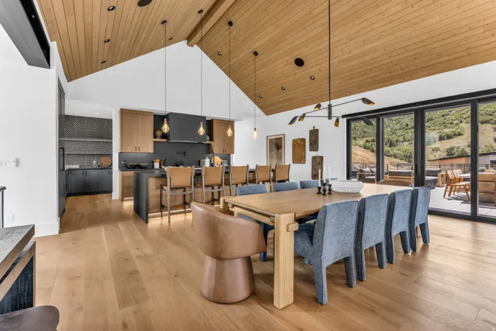 Vaulted wood-paneled ceiling, light wood-finish flooring, full wall of glass patio doors, kitchen island with seating, and integrated wet bar