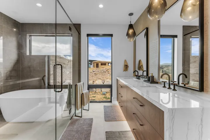 Freestanding soaking tub, glass-enclosed shower, dual vanity with undermount sinks, quartz countertop, and large format tile flooring