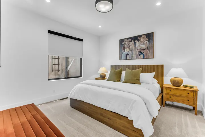 Recessed lighting and a modern ceiling fixture illuminate a bedroom with light-colored carpeting